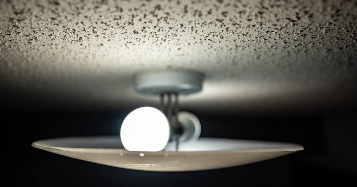 A close-up of a dual LED bulb light fixture with a glass cover mounted on a speckled popcorn ceiling