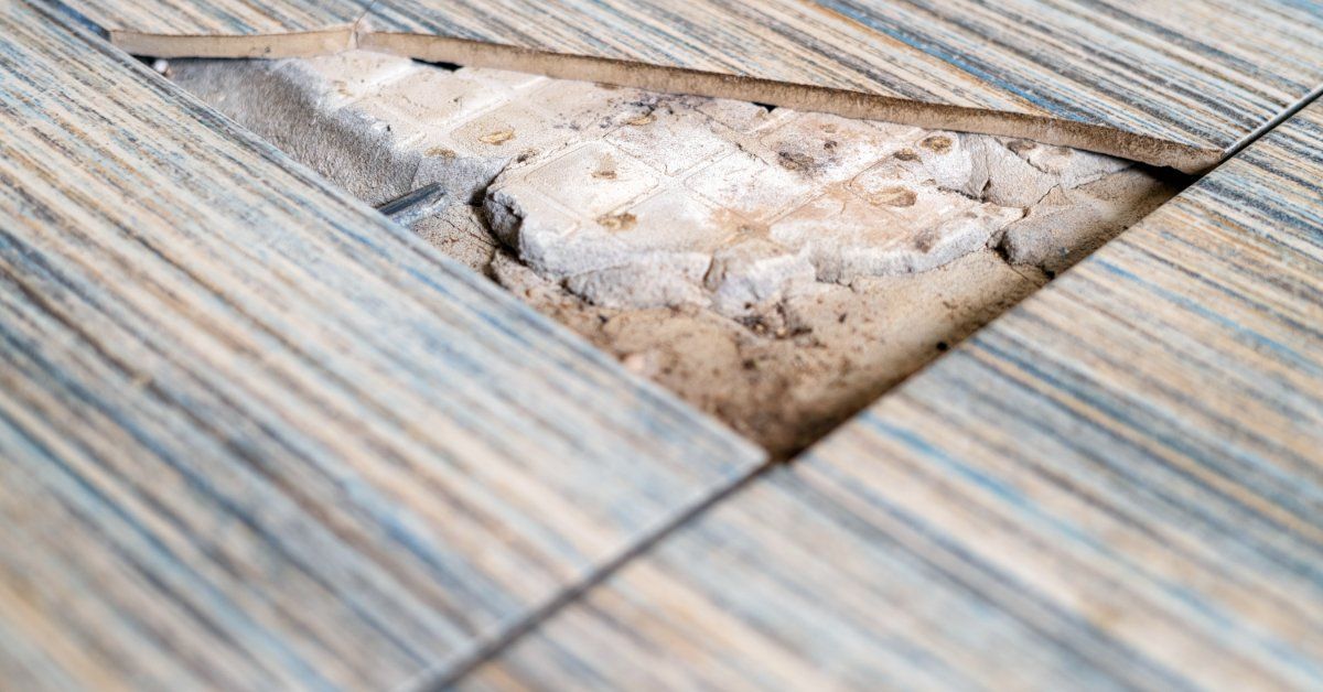 An extreme close-up of a broken ceramic floor tile revealing asbestos and surrounding damage to the 