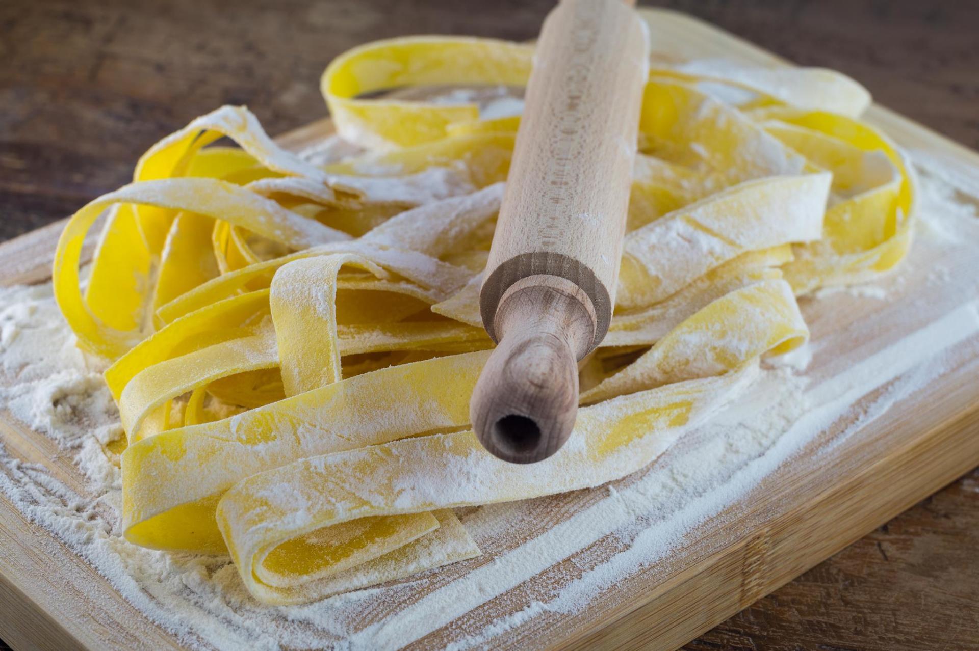 Strisce di pasta fresca stese con un mattarello di legno su un tagliere infarinato.