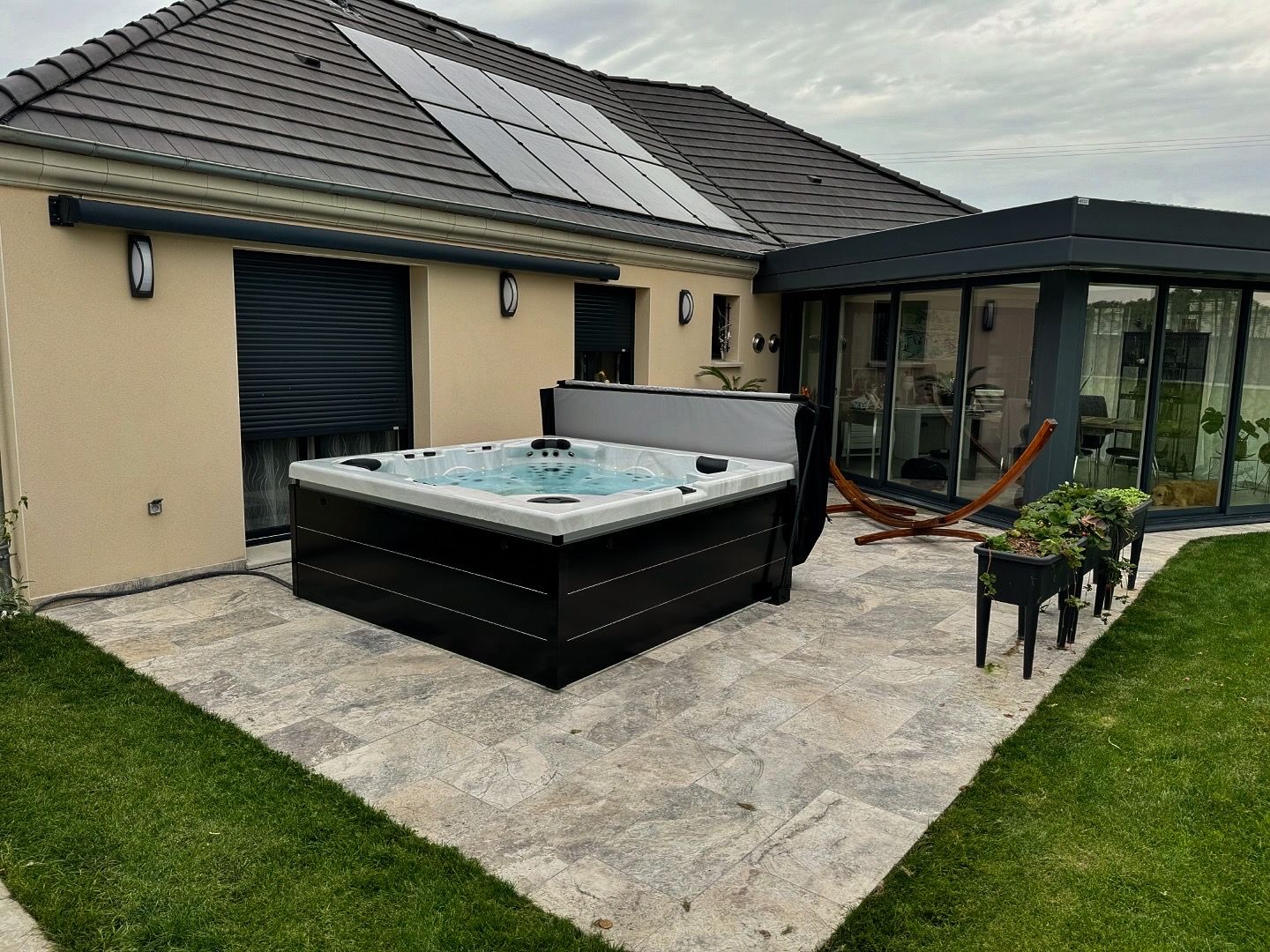 Un bain à remous est installé sur une terrasse devant une maison.