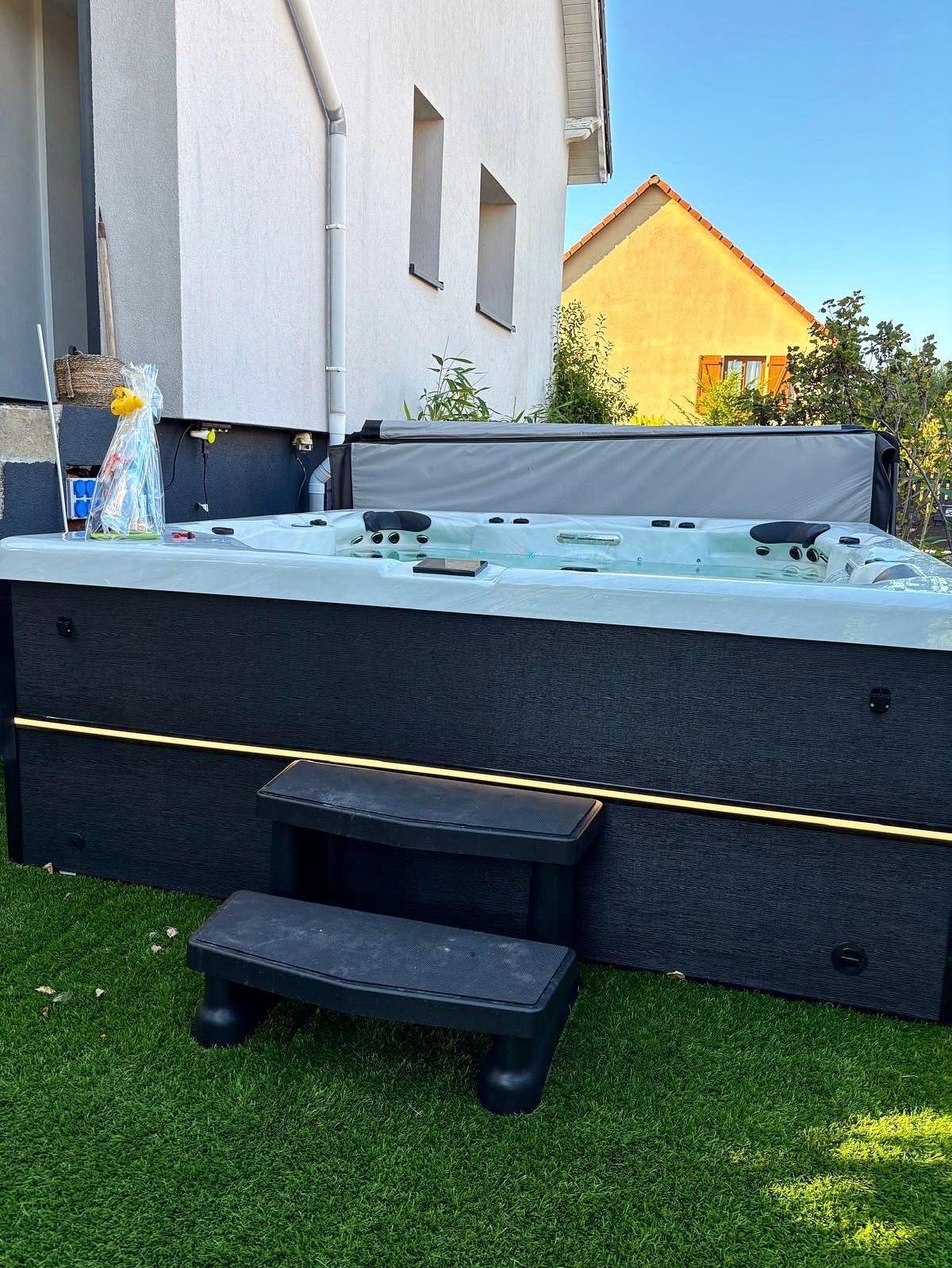 Jacuzzi noir avec marches sur gazon vert, à côté d'un bâtiment au toit jaune.