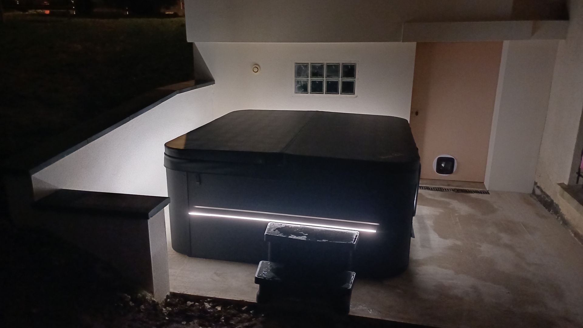 Un jacuzzi noir est éclairé la nuit devant une maison.