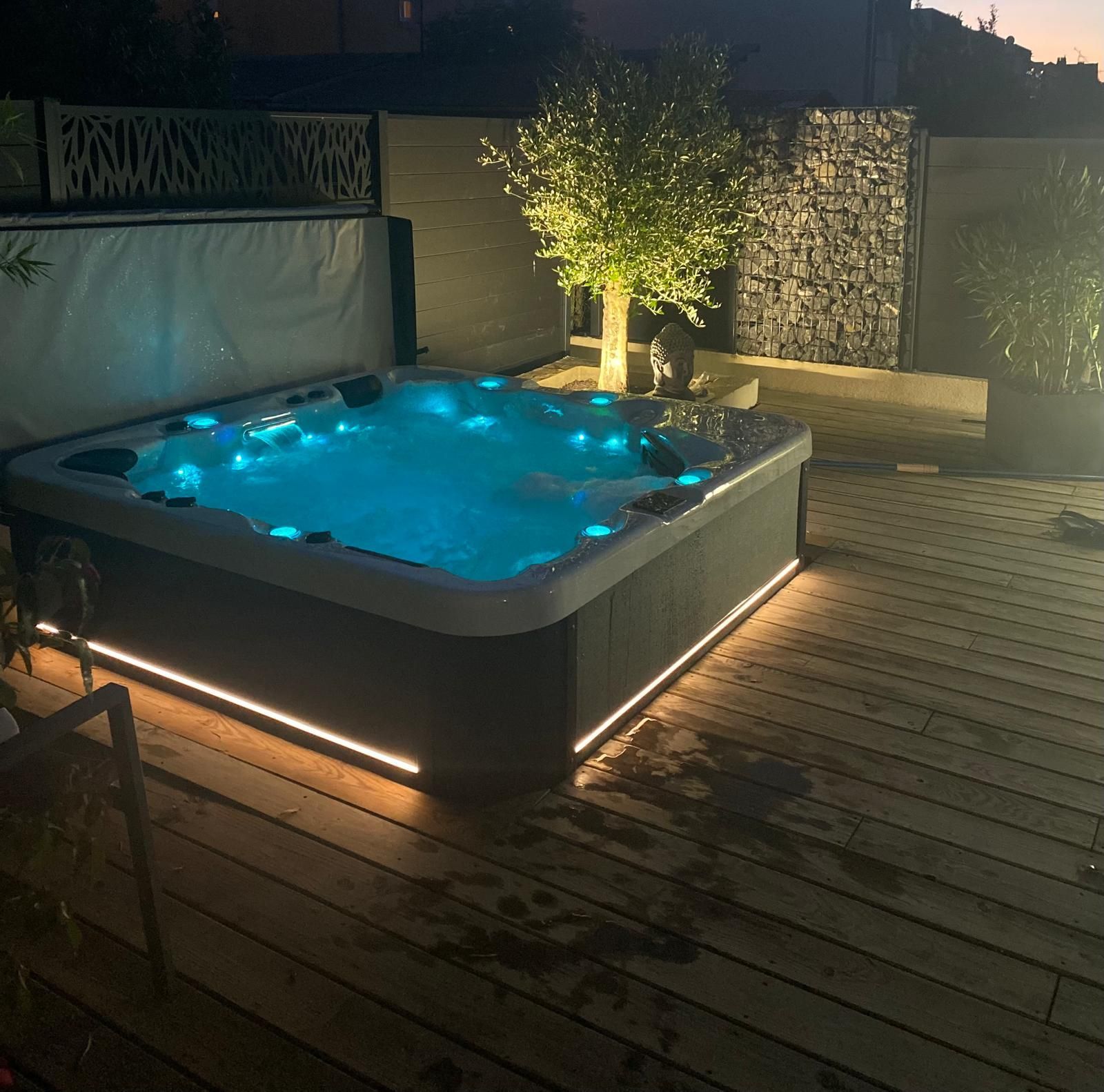 Un bain à remous est éclairé la nuit sur une terrasse en bois.