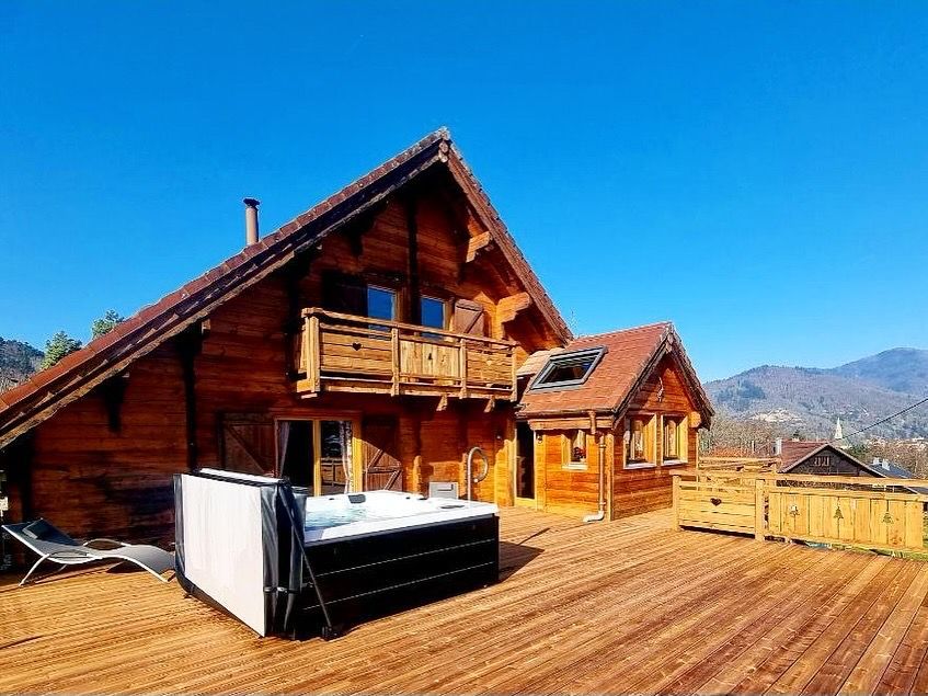 Une grande maison en bois avec un jacuzzi sur la terrasse.