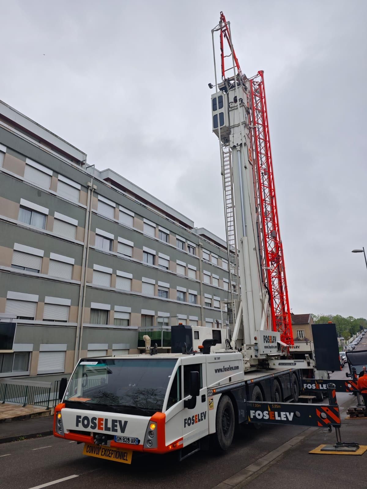 Un camion blanc avec une grue rouge à l'arrière est garé devant un bâtiment.
