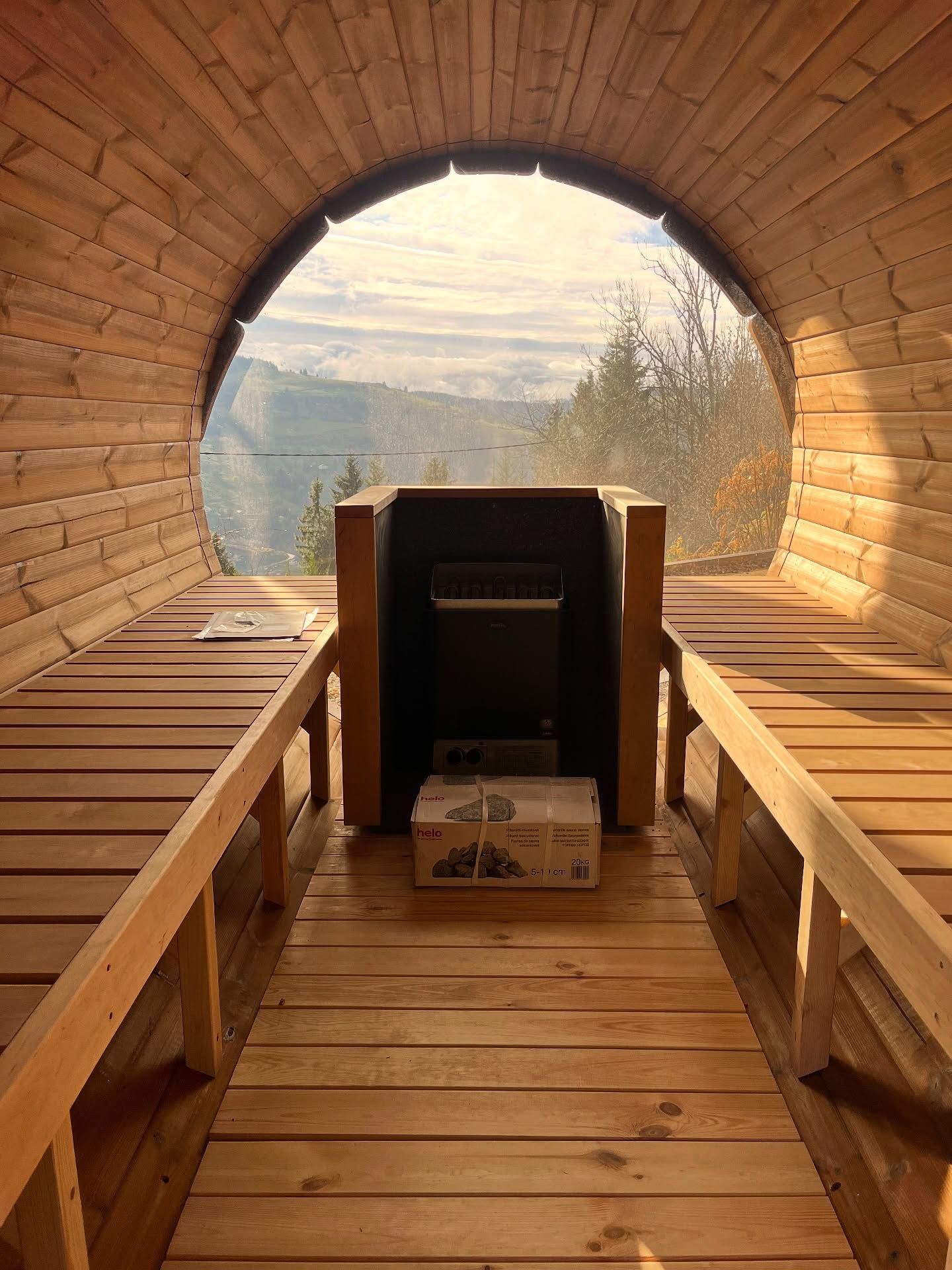 À l'intérieur d'un sauna arrondi en bois avec des bancs de chaque côté, vue sur la montagne à travers une grande fenêtre circulaire.