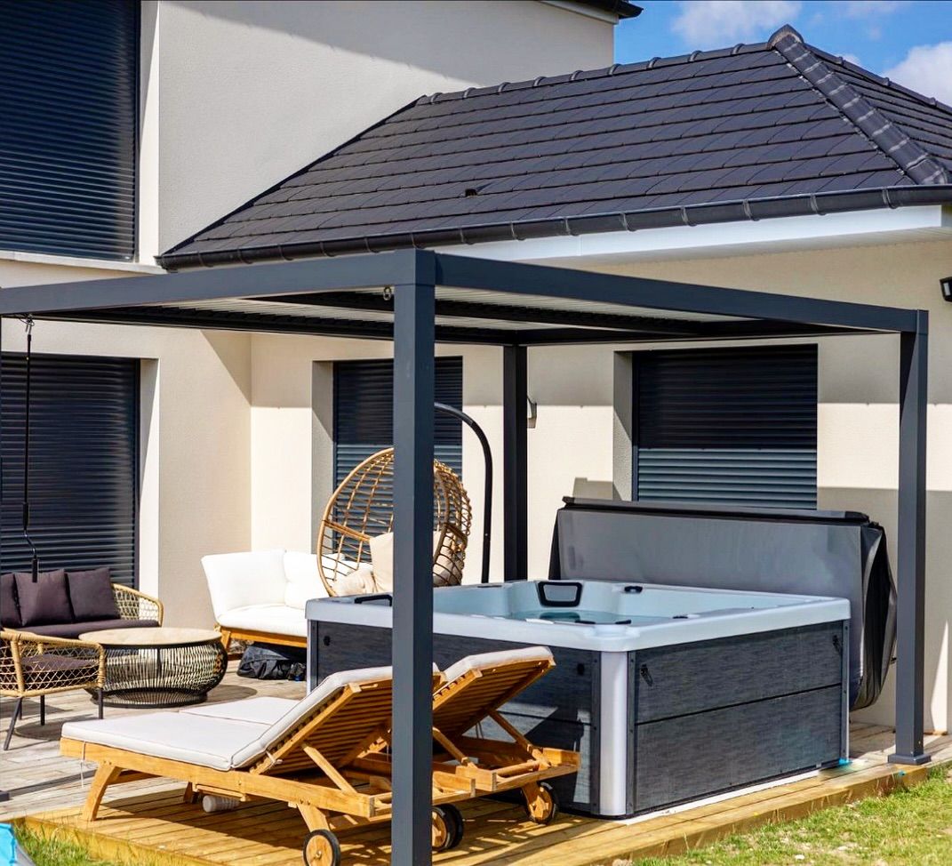 Un espace patio comprend un jacuzzi gris sous une pergola, avec des chaises longues en bois, un fauteuil suspendu et du mobilier de jardin.