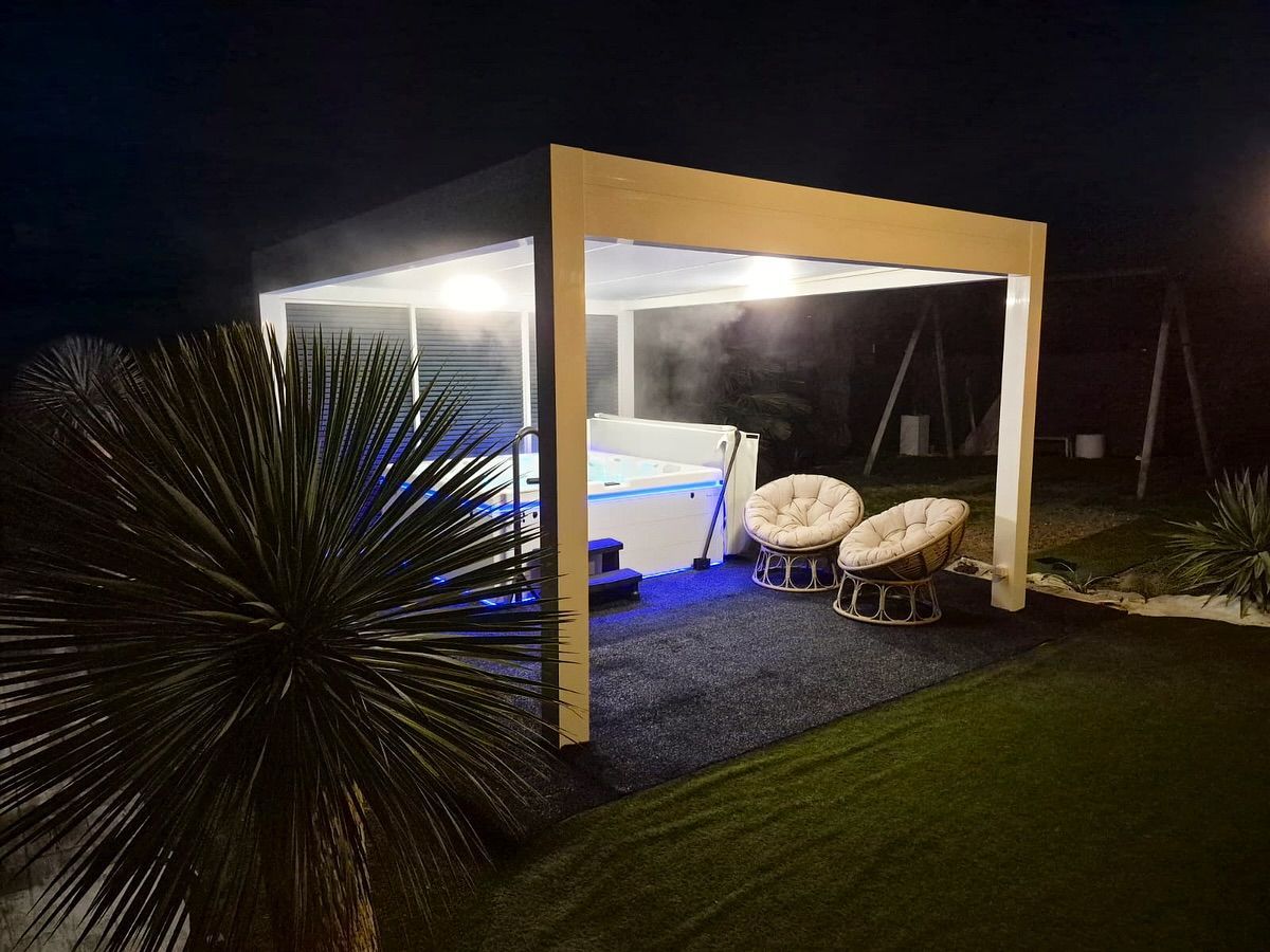 La nuit, un kiosque blanc éclairé de l'intérieur abrite un bain à remous fumant aux lumières bleues et deux chaises longues en osier.