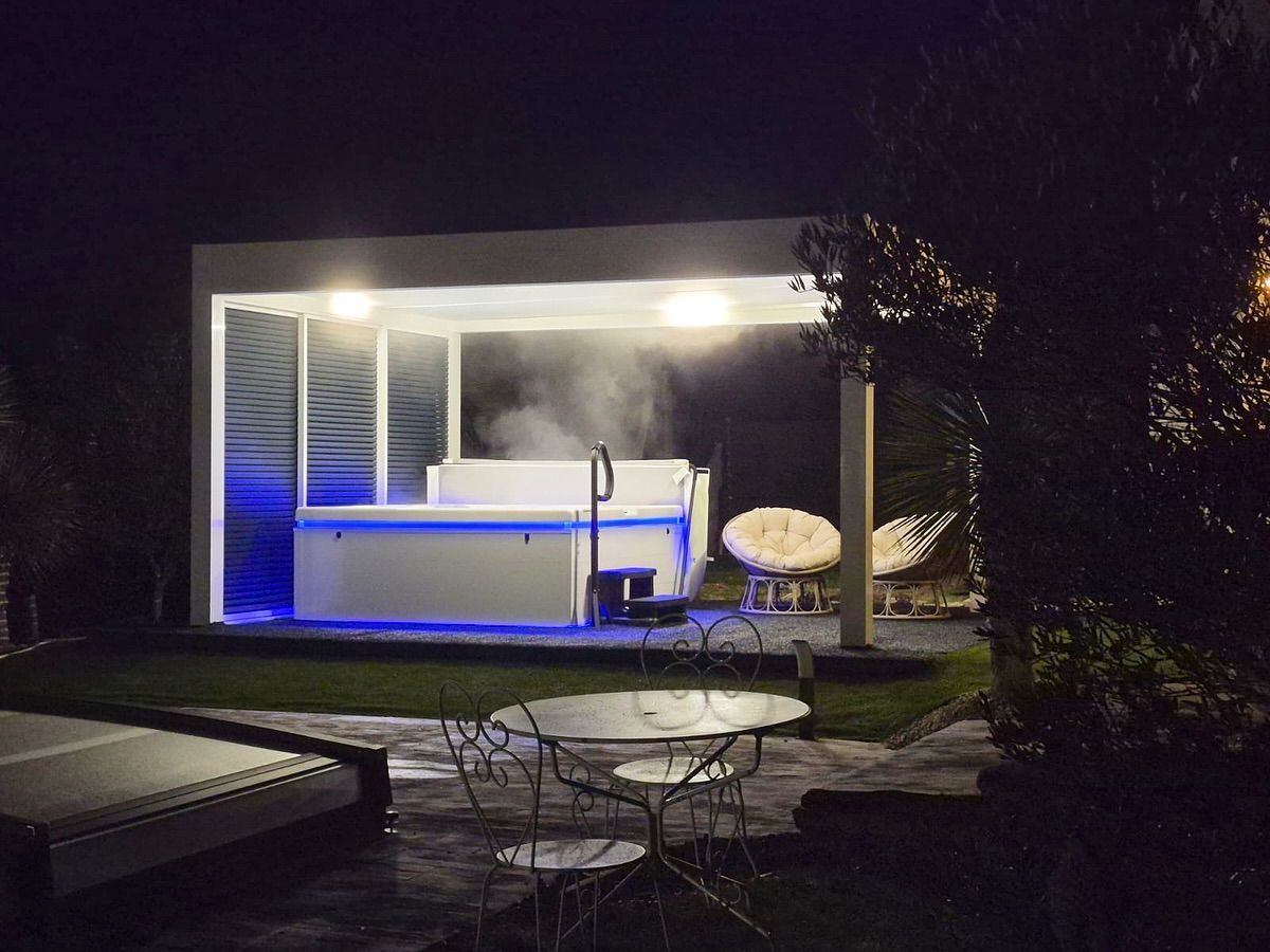 Un bain à remous fumant sous une pergola éclairée, la nuit, avec un salon de jardin au premier plan.