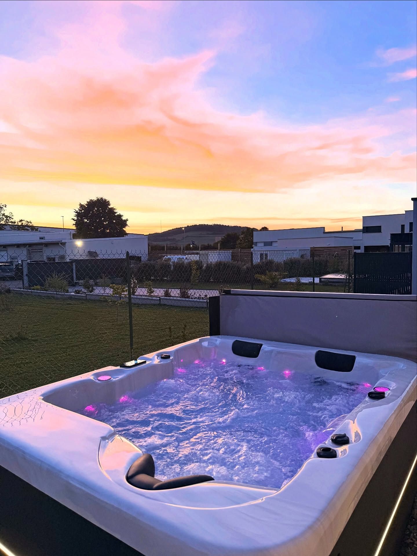 Au coucher du soleil, un jacuzzi illuminé trône dans un jardin gazonné, avec son eau bleue bouillonnante et son éclairage d'ambiance violet.