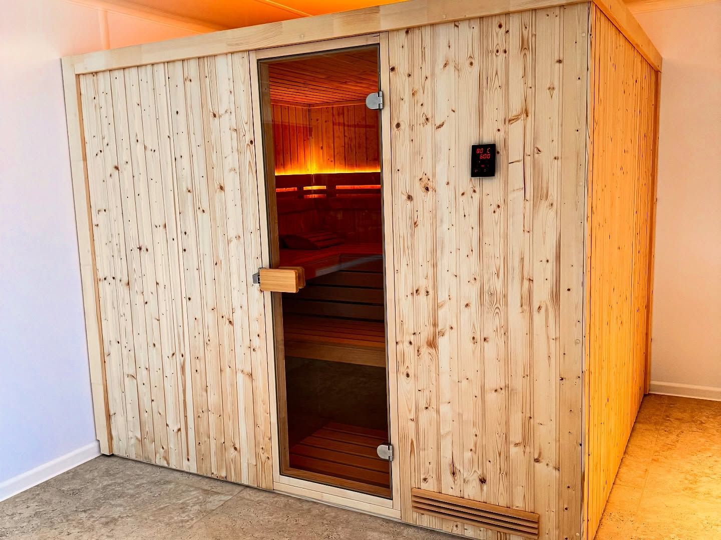 Une cabine de sauna en bois avec une porte vitrée dans une pièce au sol clair.