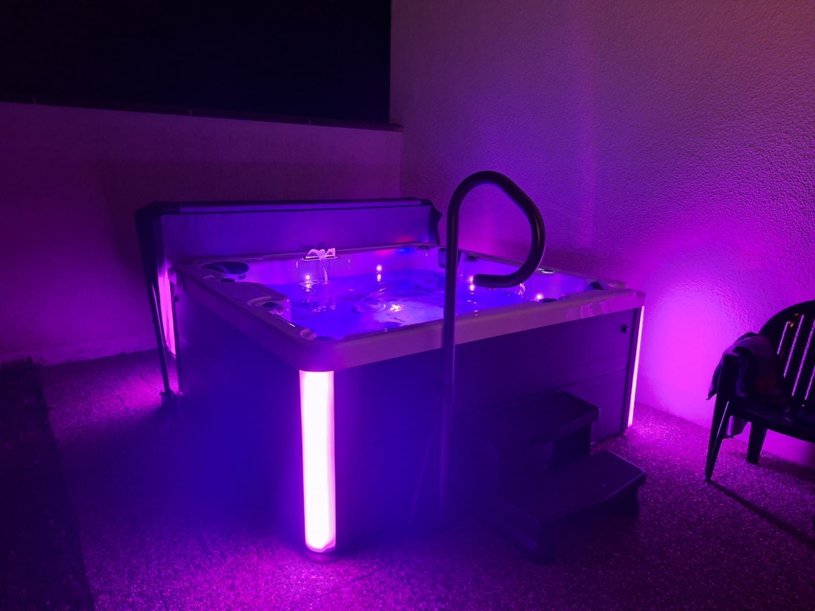 Un bain à remous est éclairé par des lumières violettes dans une pièce.