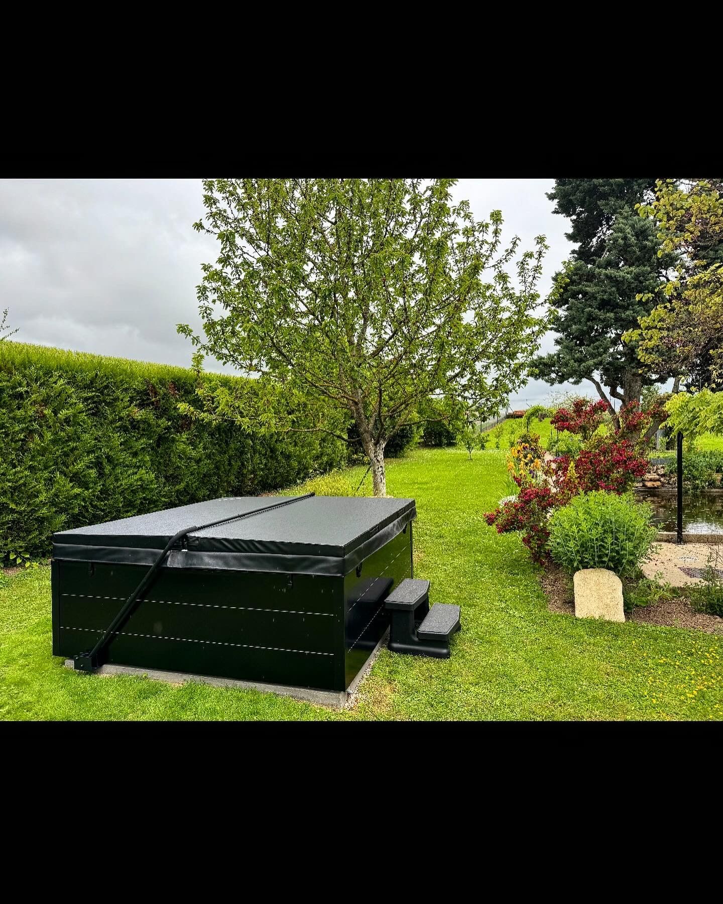 Un jacuzzi noir se trouve au milieu d'une cour verdoyante.