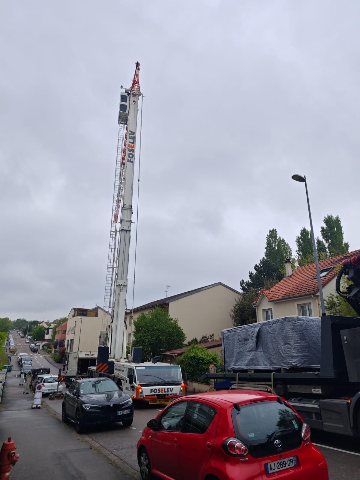 Une voiture rouge est garée sur le bord de la route à côté d'une grue.