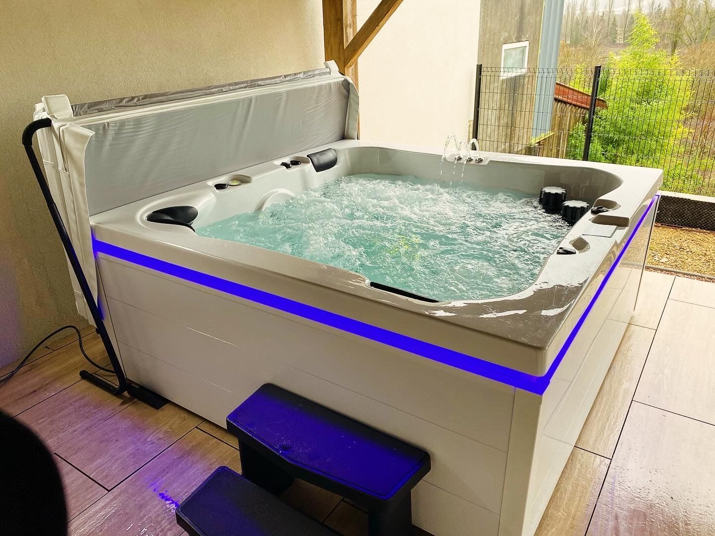 Un jacuzzi blanc avec des lumières bleues est posé sur une terrasse.