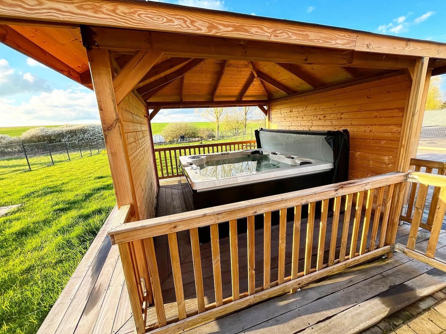 Un bain à remous est installé sous un belvédère sur une terrasse en bois.
