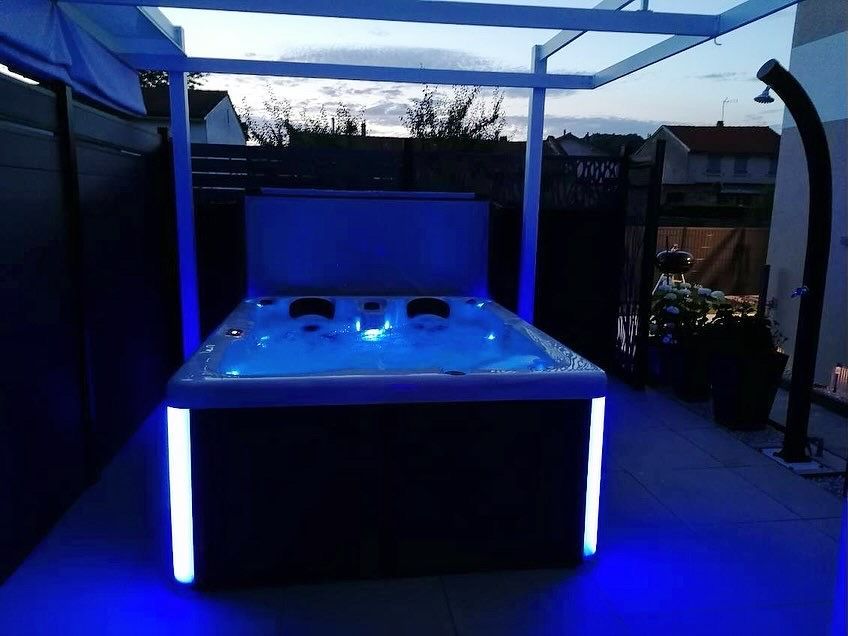 Un bain à remous avec des lumières bleues est assis sous un auvent sur une terrasse.