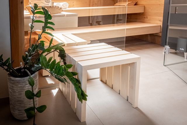 Un banc en bois dans un sauna à côté d'une plante en pot.
