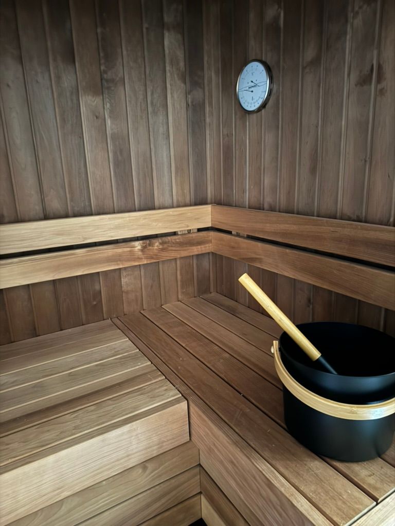 Un seau noir avec une poignée en bois est posé sur un banc en bois dans un sauna en bois.