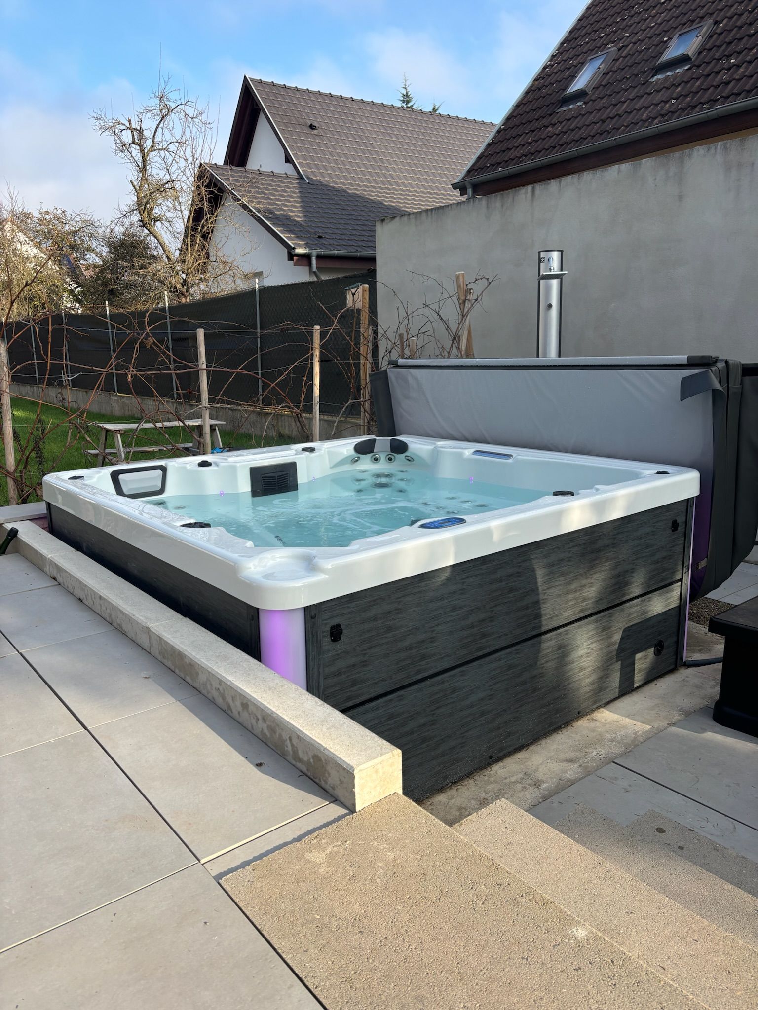 Un grand bain à remous est installé sur une terrasse à côté d'une maison.
