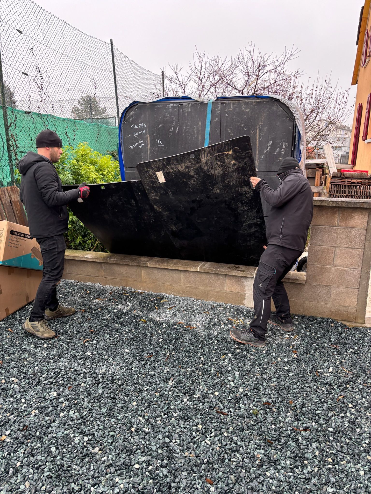 Deux hommes transportent un gros morceau de métal sur un chemin de gravier.