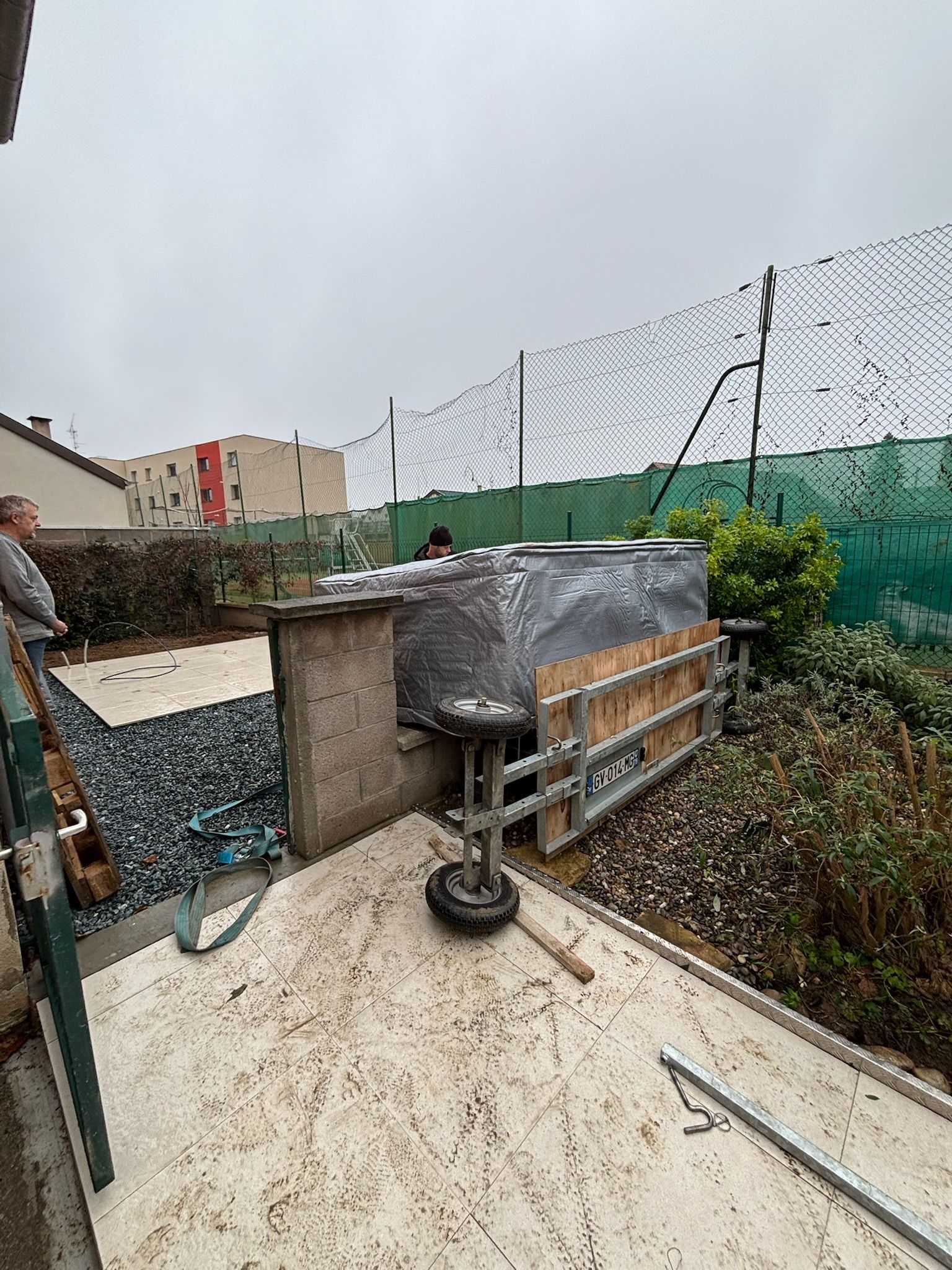 Un homme est assis sur un balcon donnant sur une cour clôturée.