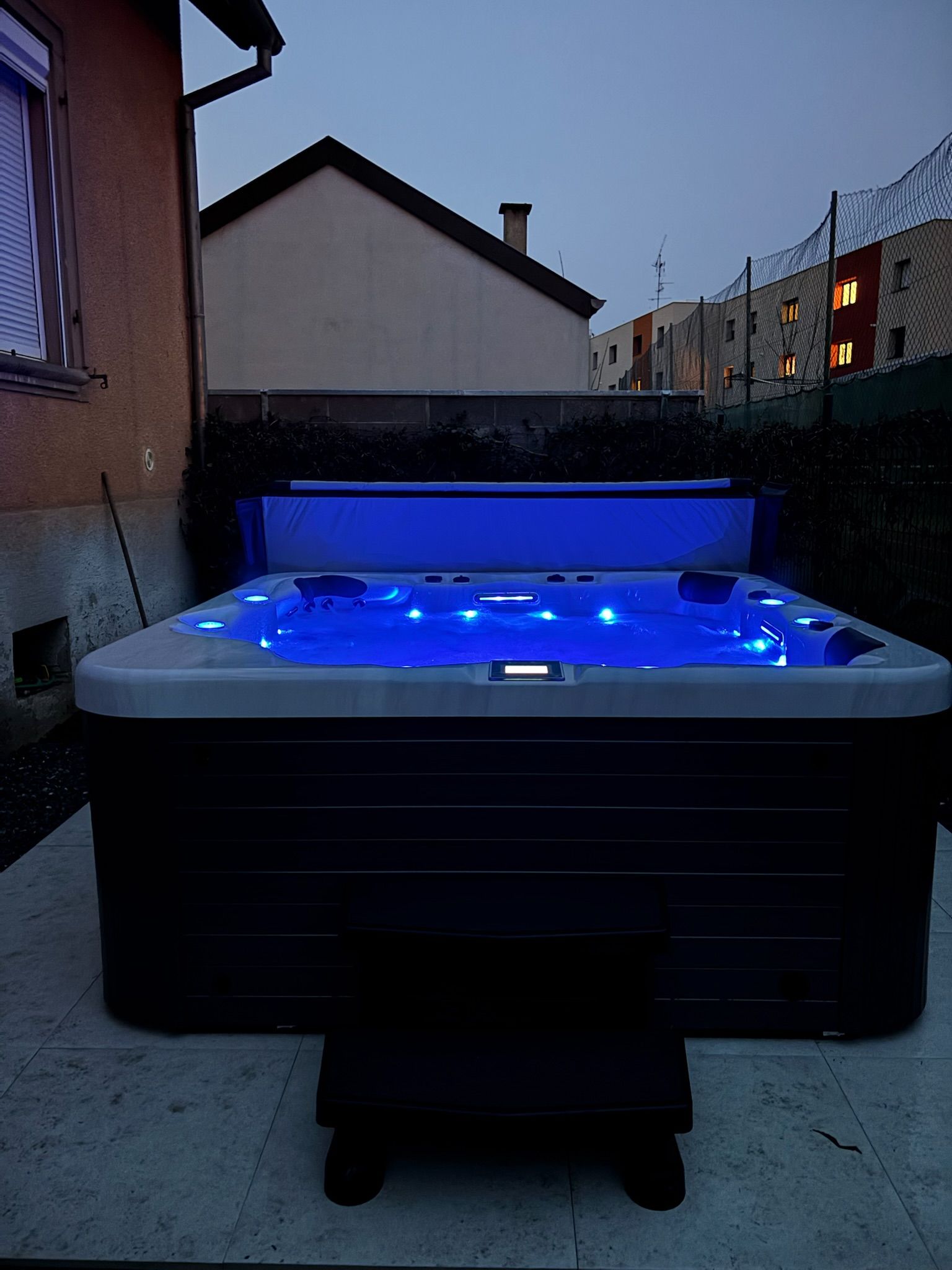 Un jacuzzi est éclairé par des lumières bleues devant une maison