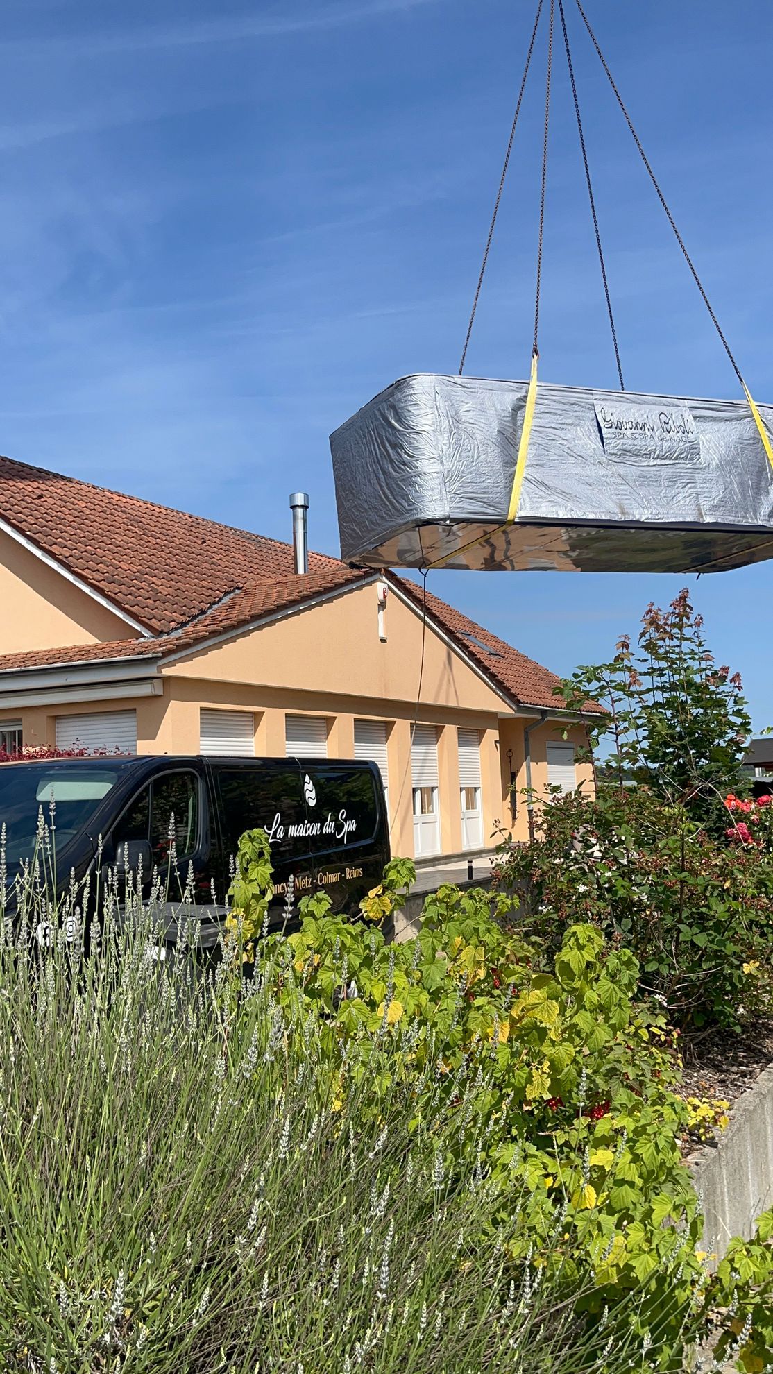 Un gros morceau de métal est soulevé par une grue devant une maison.