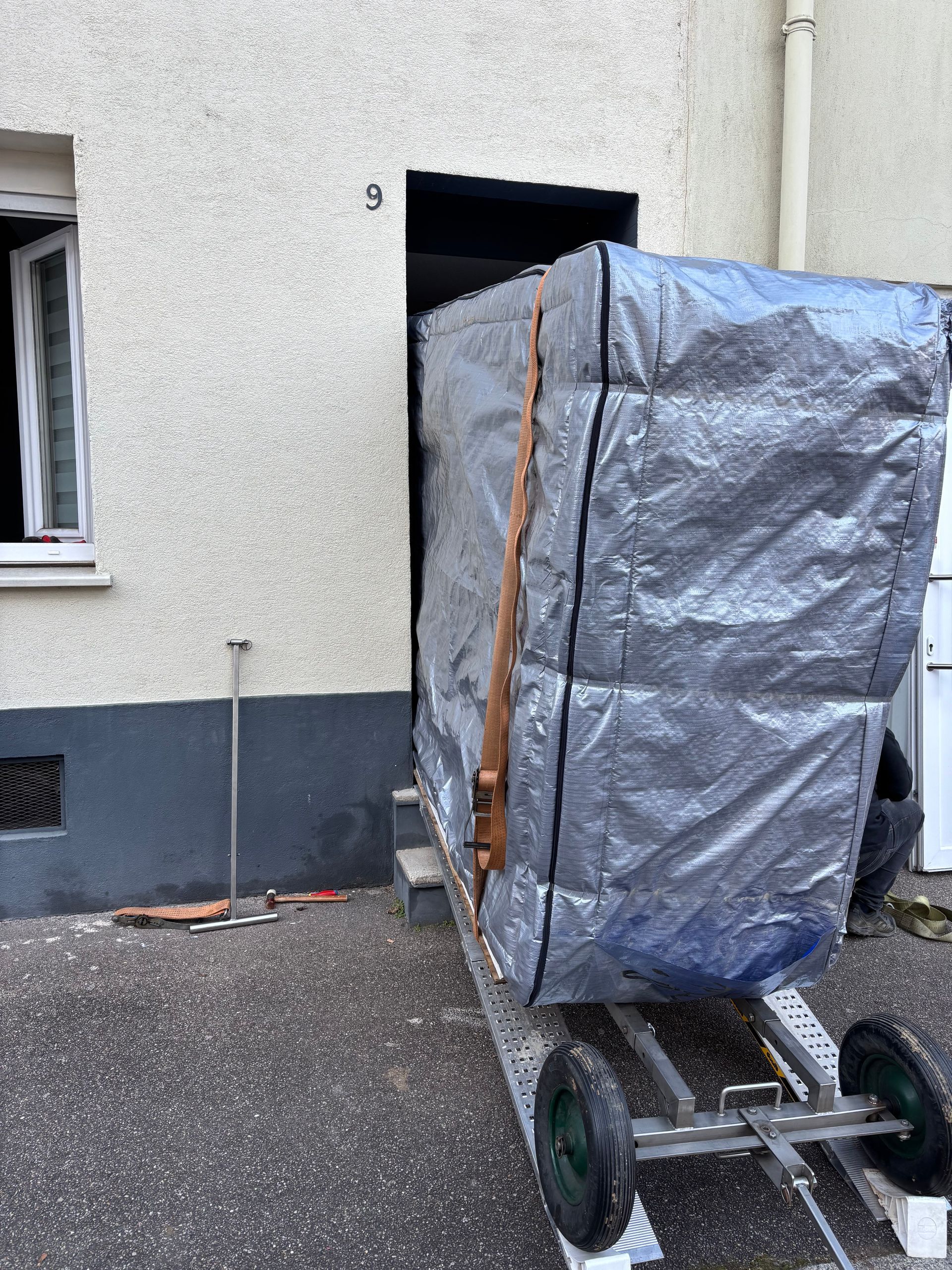 Un gros meuble est posé sur une remorque devant un bâtiment.