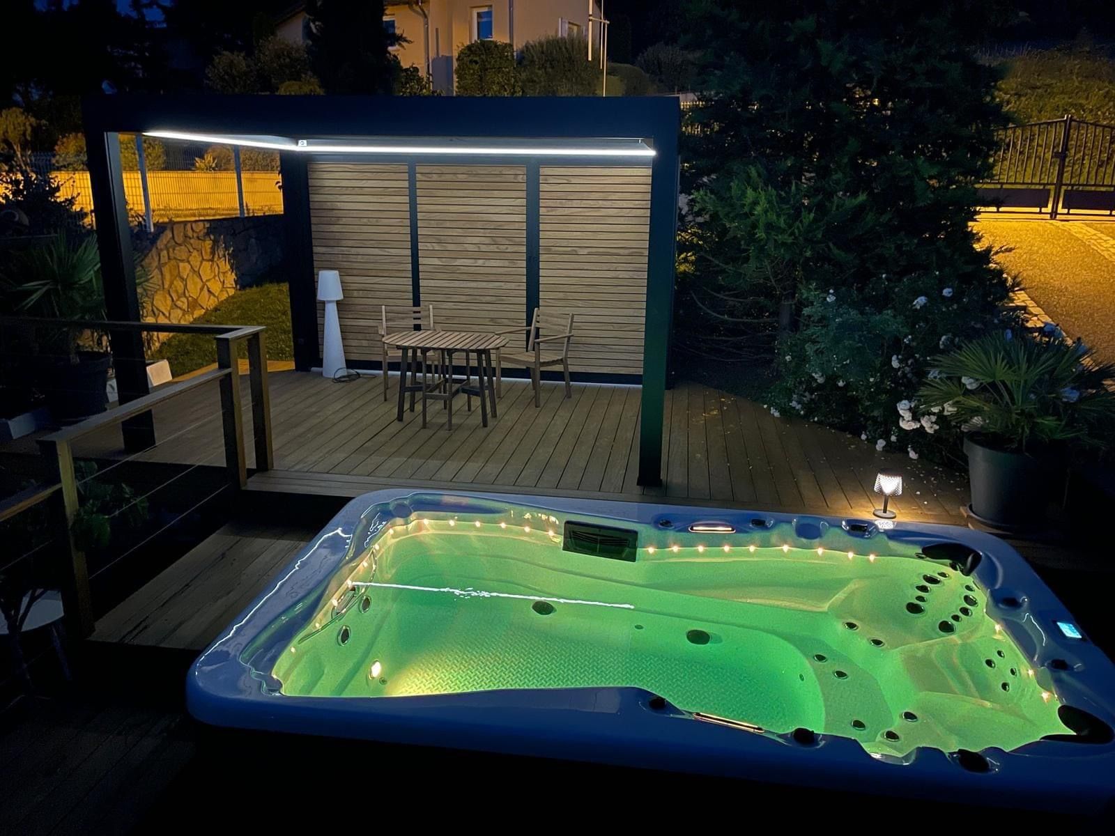 Un bain à remous avec des lumières vertes se trouve sur une terrasse la nuit.