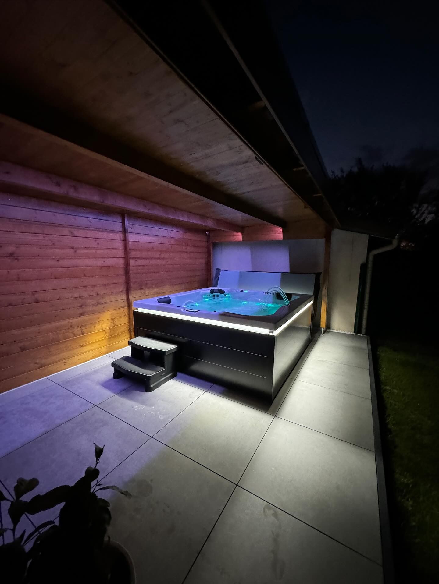 Un bain à remous est installé sur une terrasse sous un toit en bois la nuit.