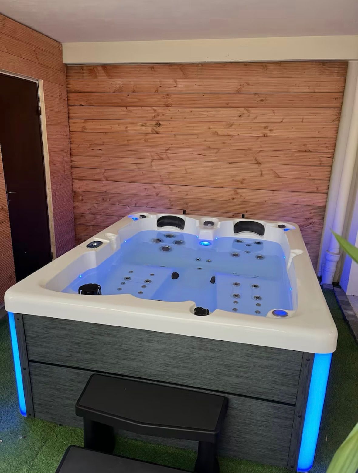 Un grand bain à remous est installé dans une pièce à côté d'un mur en bois.