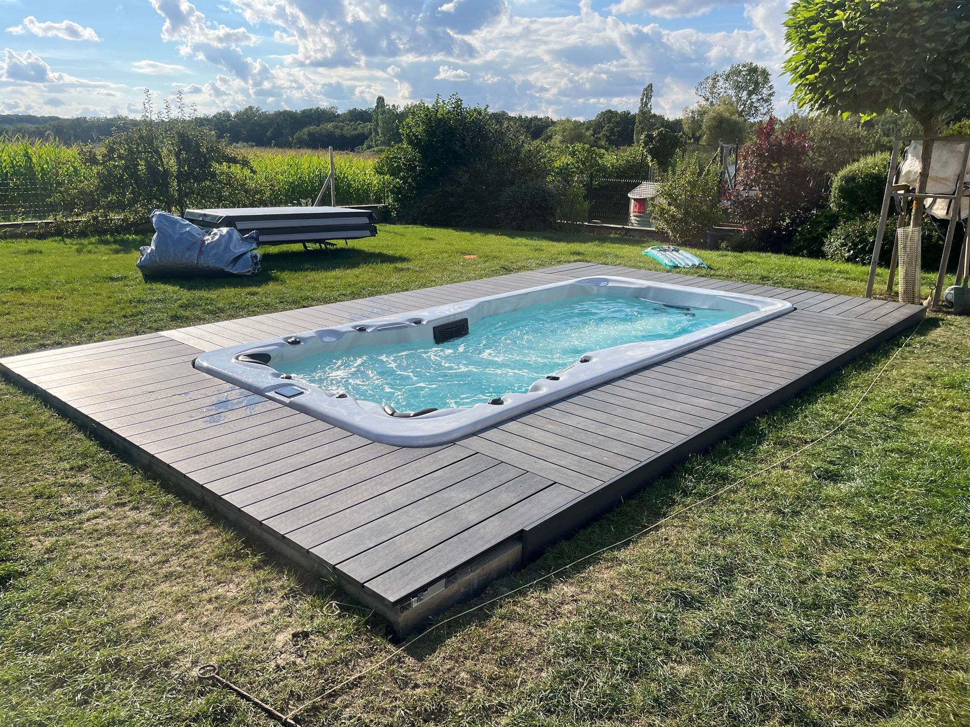 Une piscine est située sur une terrasse en bois au milieu d'un champ verdoyant.