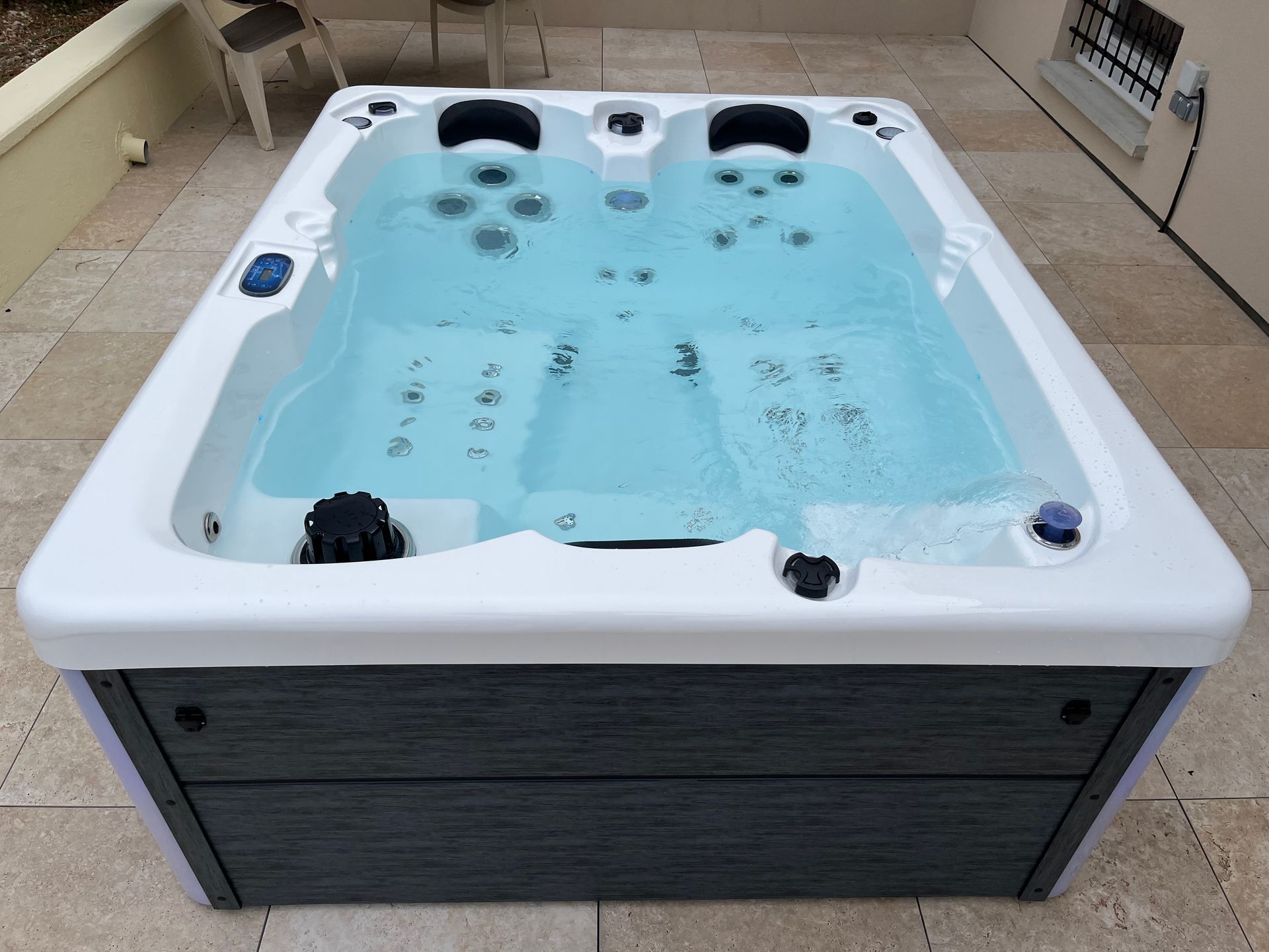 Un jacuzzi rempli d'eau sur une terrasse. Il est blanc avec un extérieur gris.