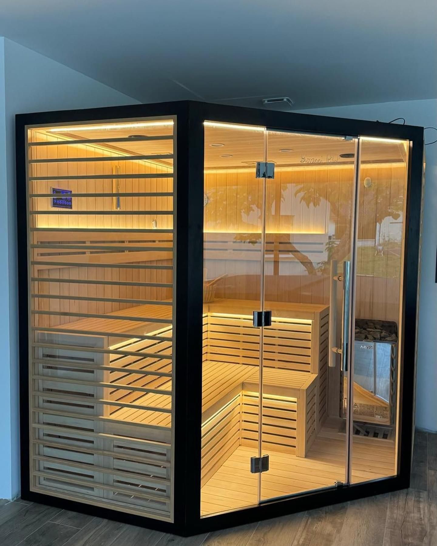 Un grand sauna en bois avec une porte vitrée se trouve dans une pièce.