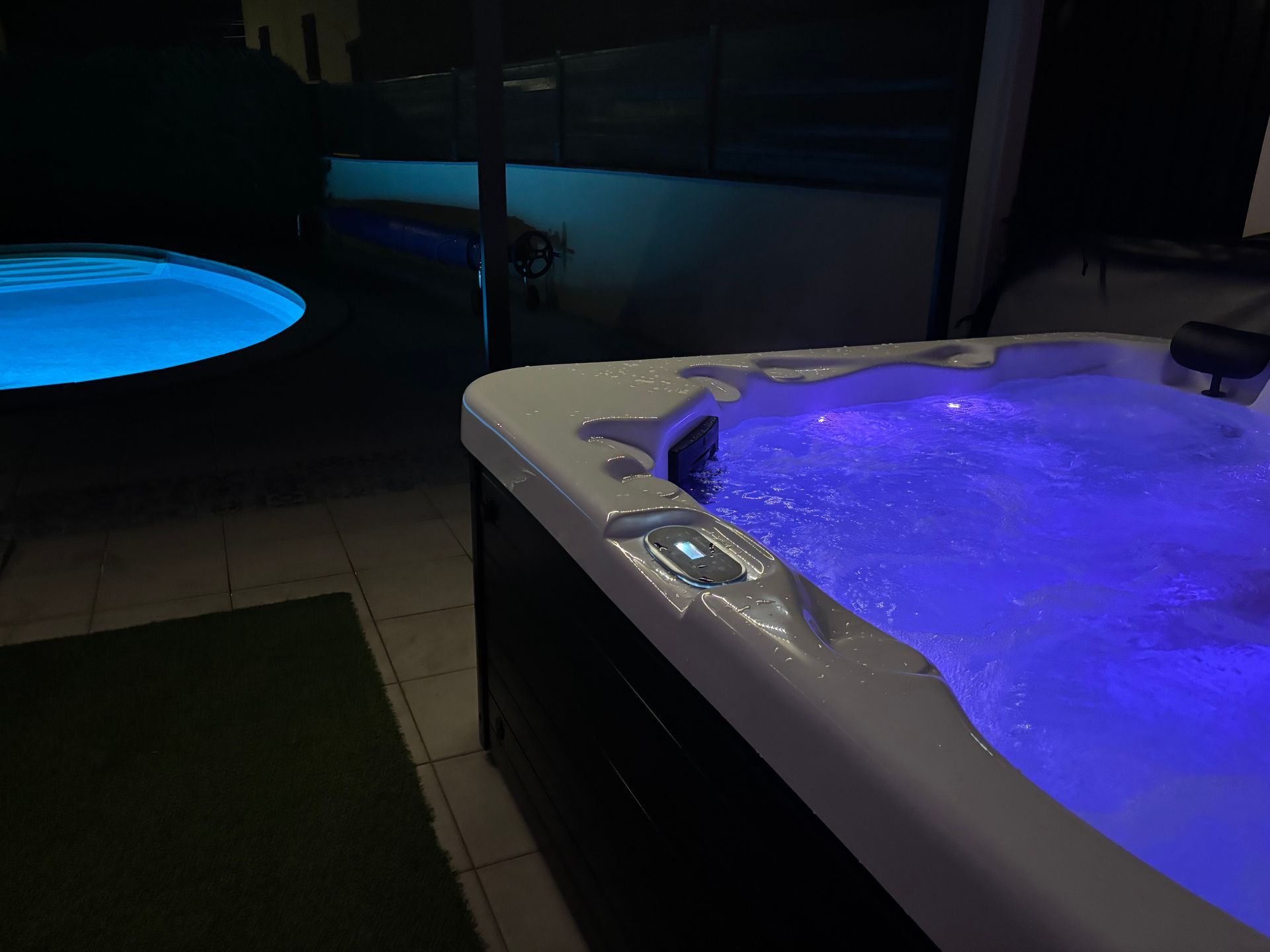Bain à remous avec lumières bleues à côté d'une piscine la nuit.