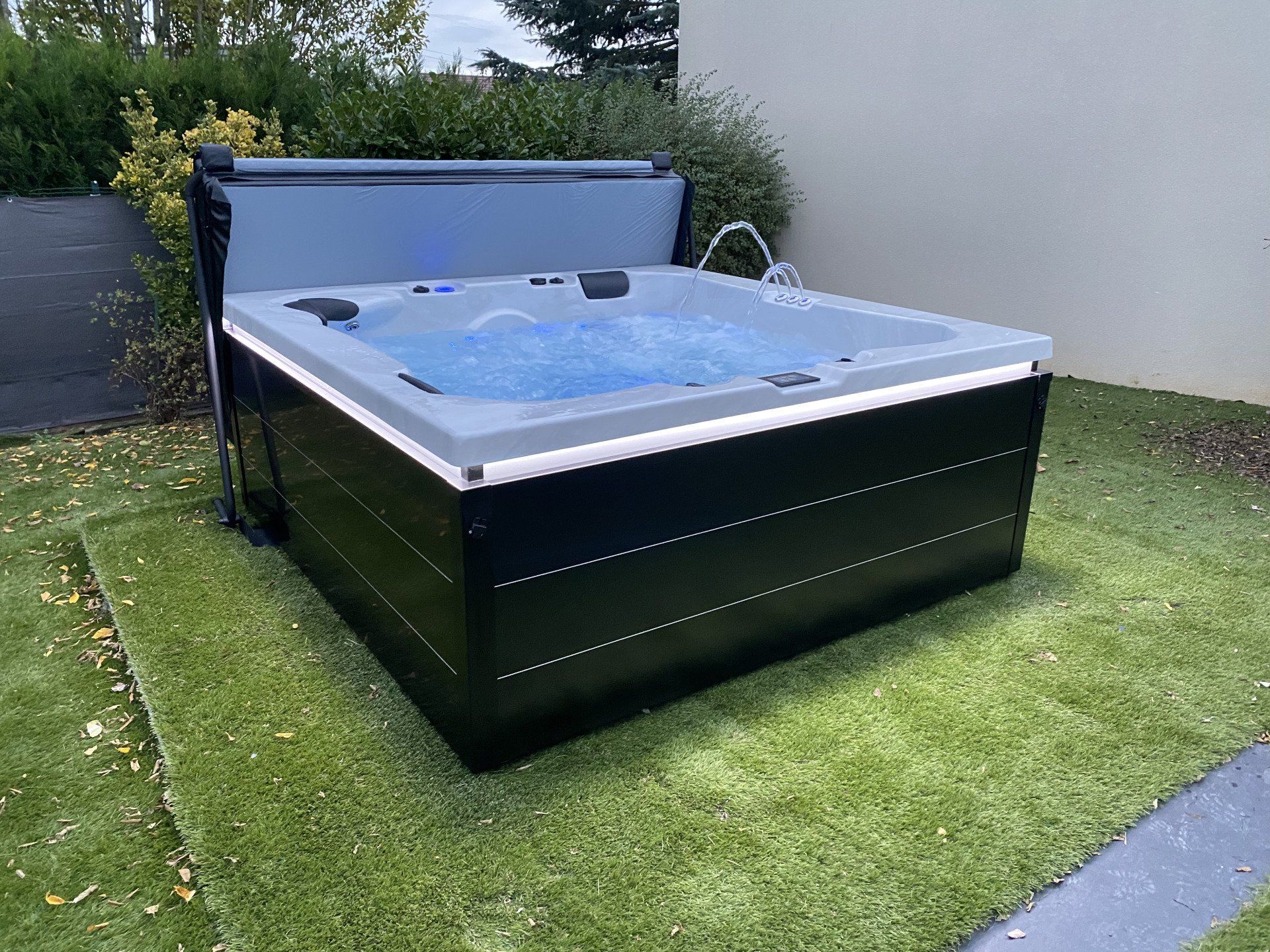 Un jacuzzi noir et gris est posé sur une pelouse verte luxuriante.