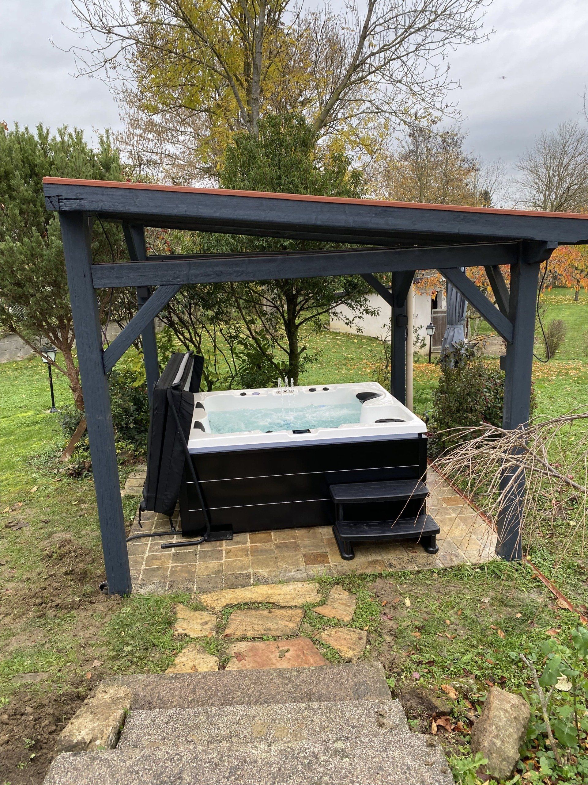 Un bain à remous est installé sous une pergola dans un jardin.
