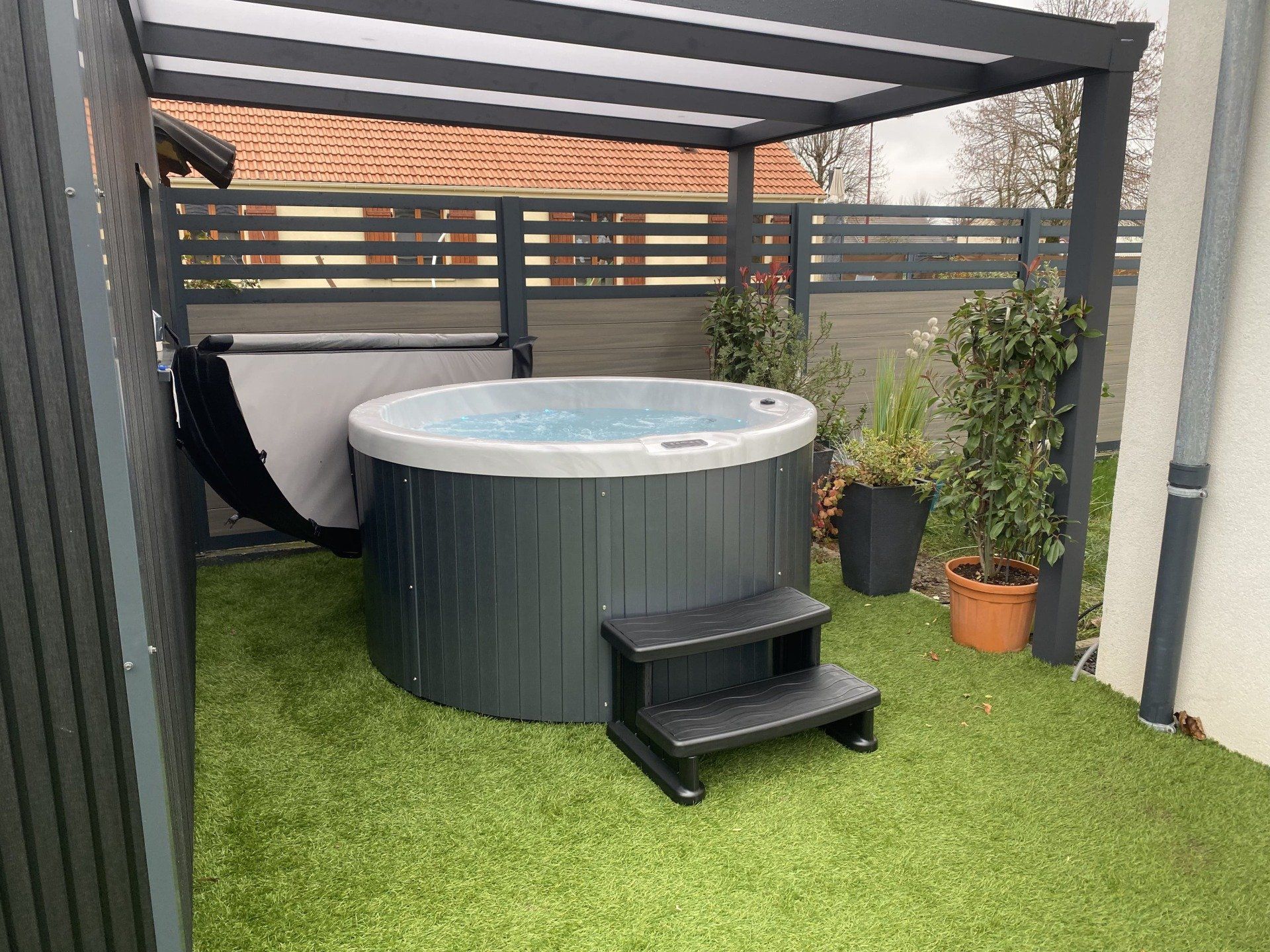 Un bain à remous est posé sur une pelouse verte luxuriante sous un auvent.