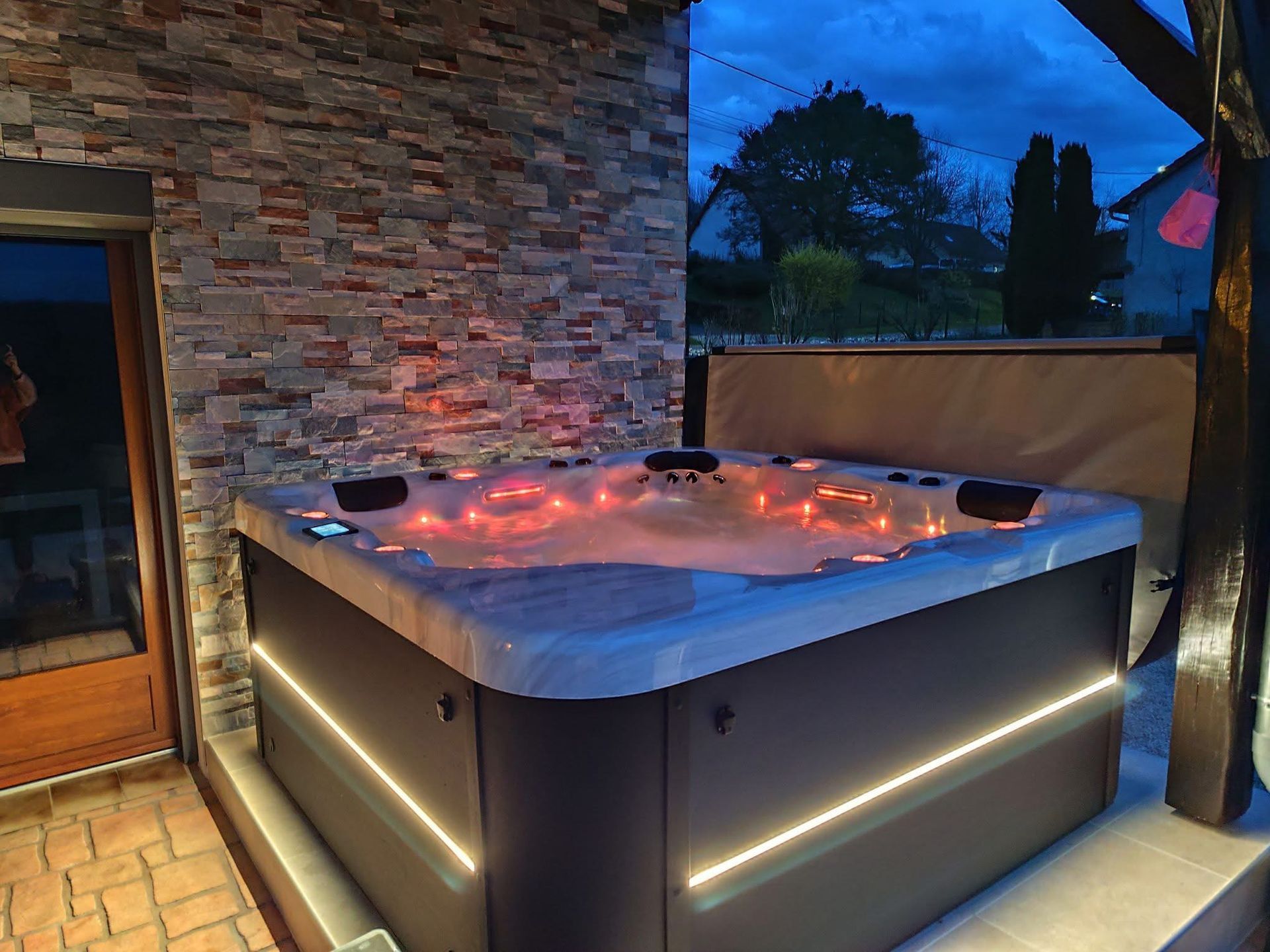 Un jacuzzi est éclairé la nuit devant un mur de pierre.