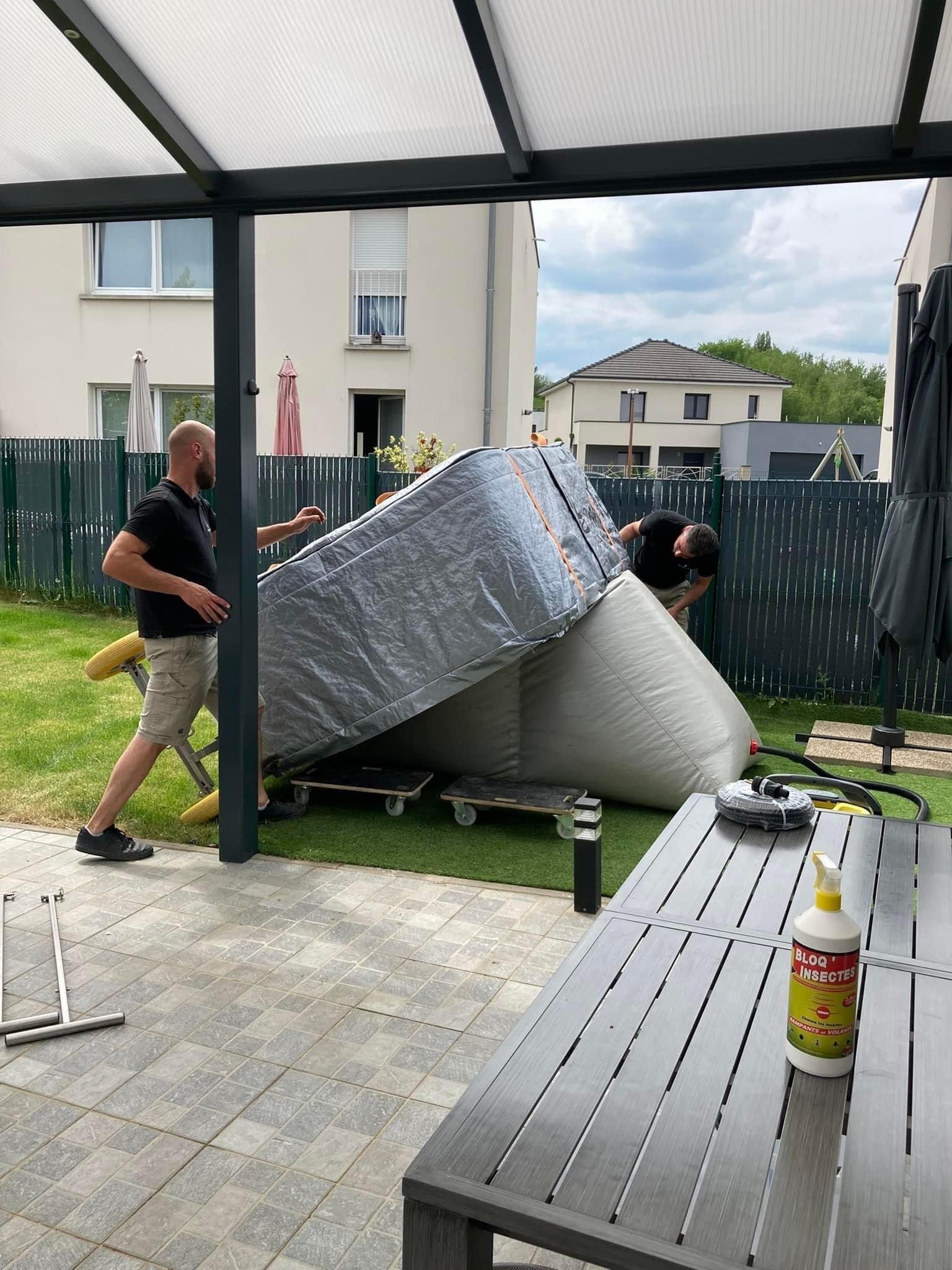 Deux hommes transportent un gros meuble sur une terrasse.