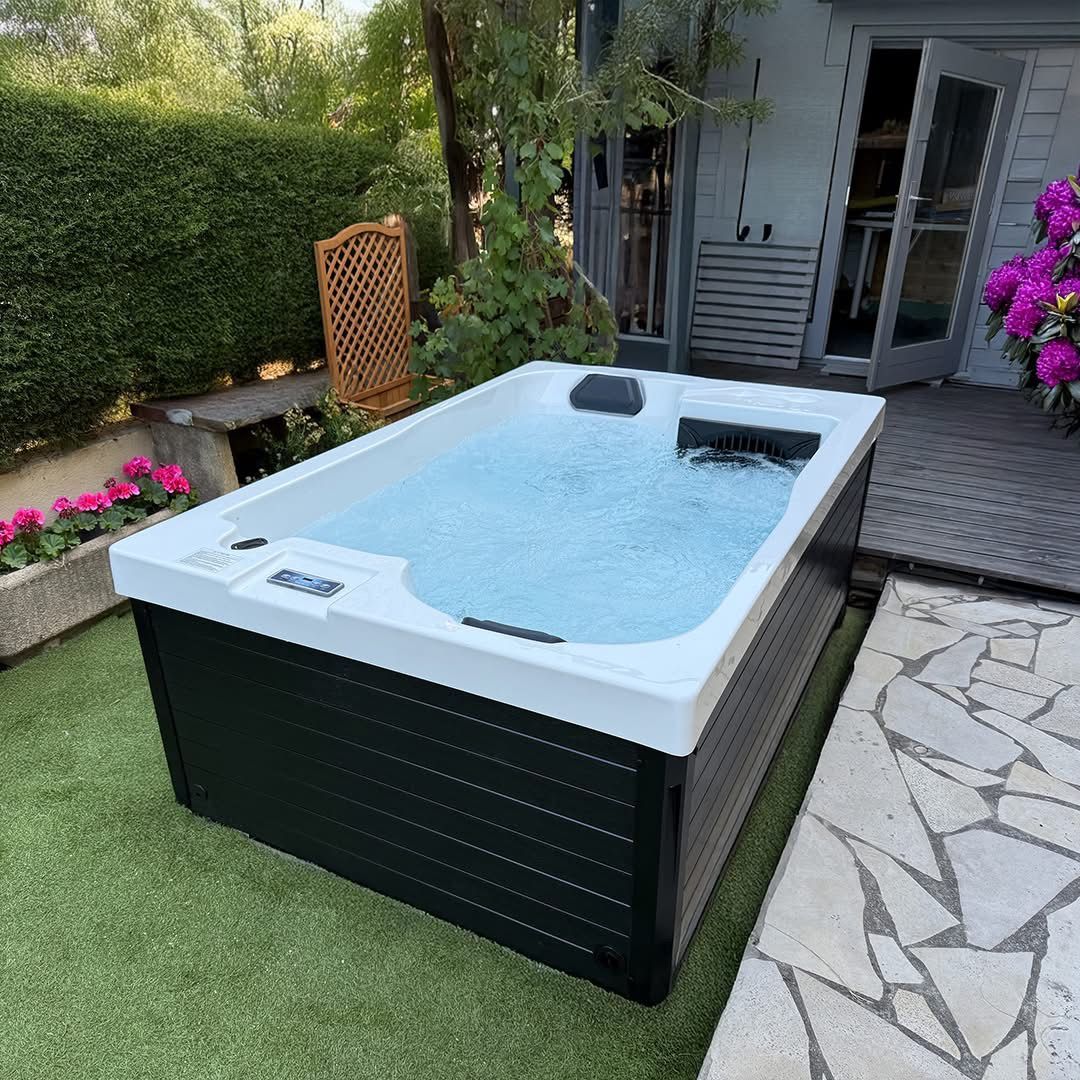 Un jacuzzi blanc et noir est posé sur une pelouse verte luxuriante.