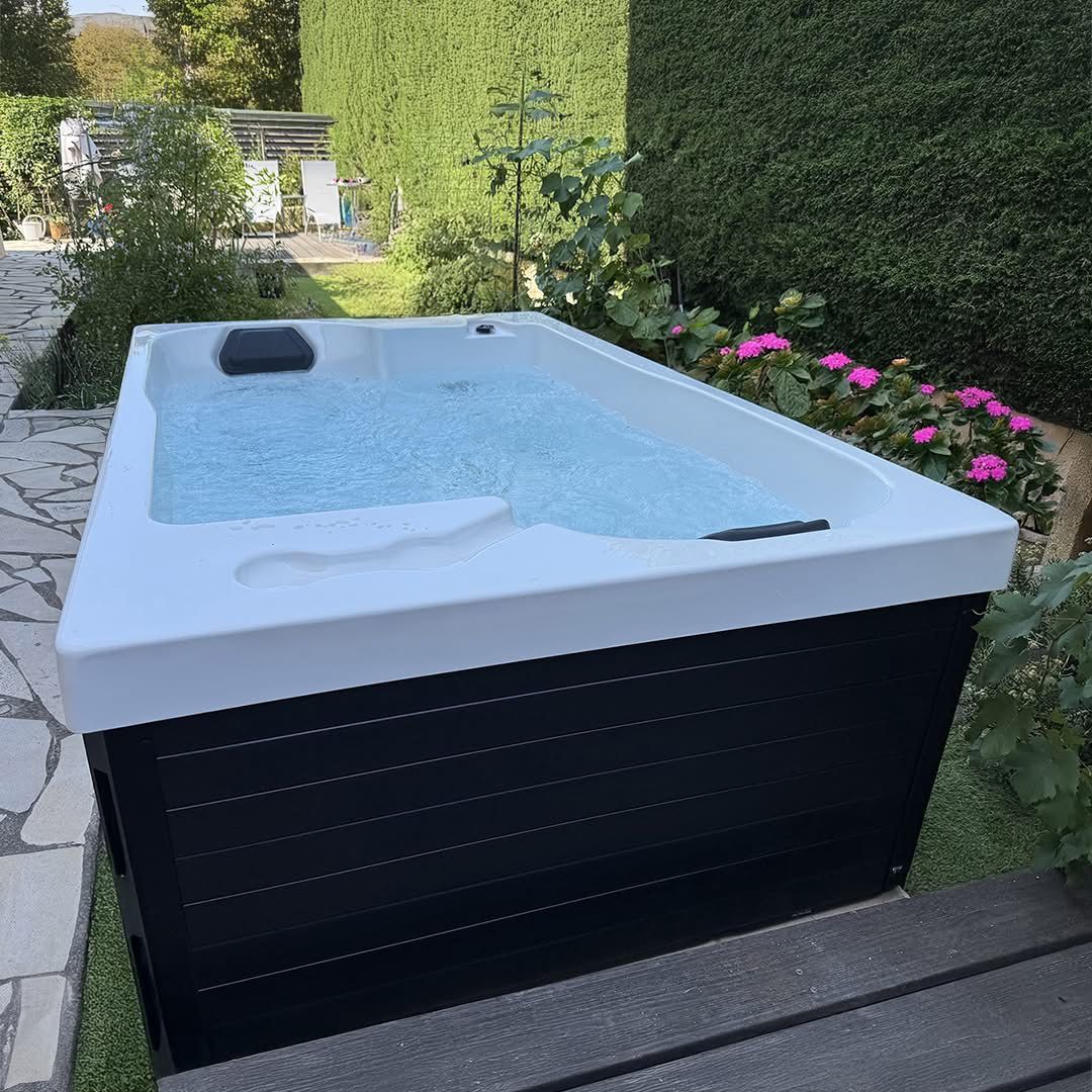 Un jacuzzi blanc et noir est posé sur une terrasse en bois dans un jardin.