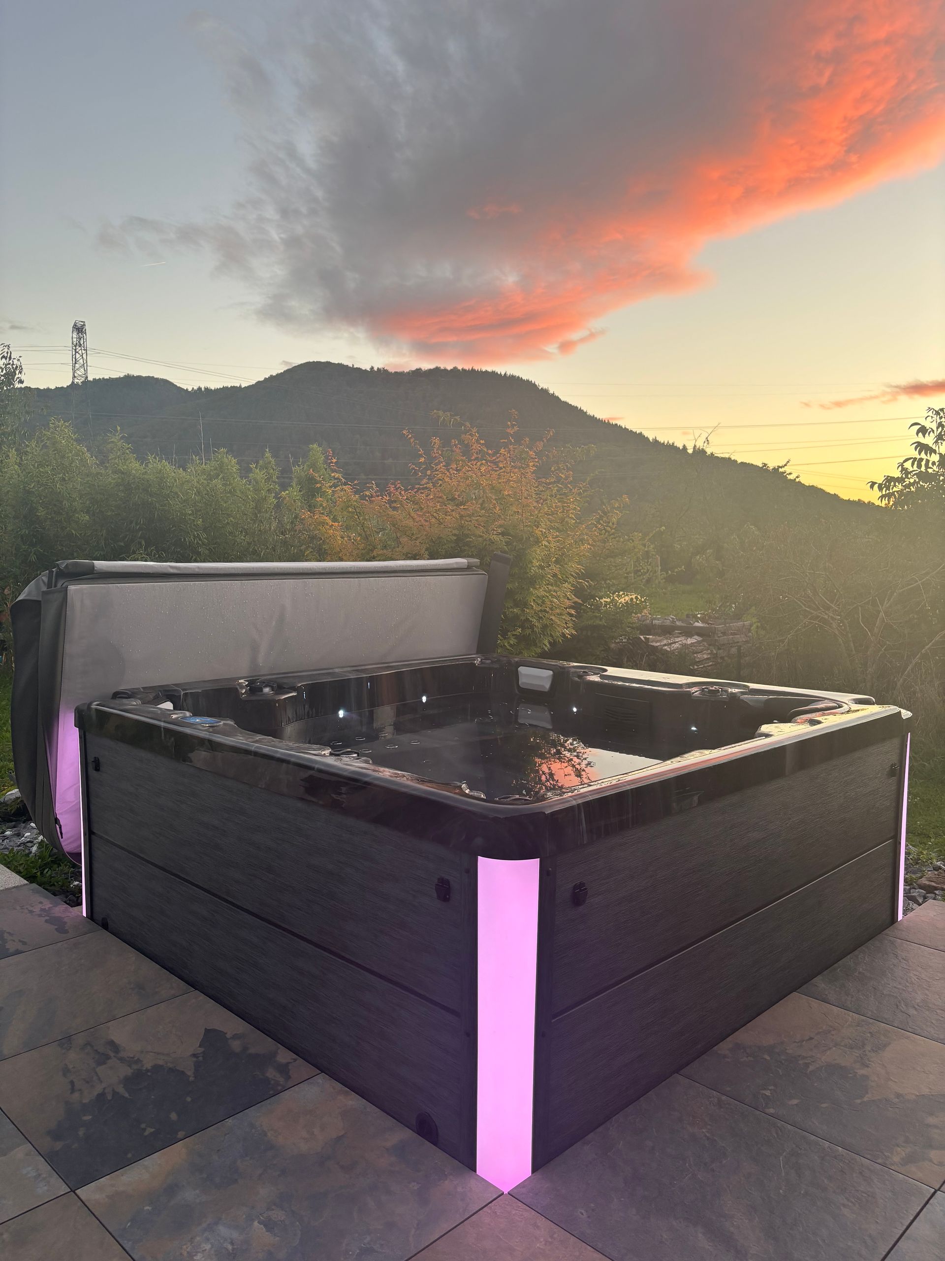 Spa illuminé en rose, extérieur avec vue sur la montagne au coucher du soleil.