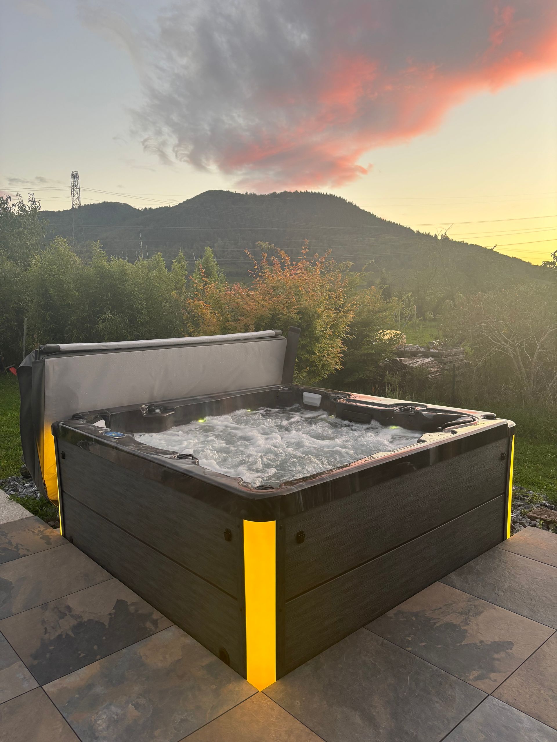 Bain à remous avec eau pétillante à l'extérieur, bords éclairés, toile de fond de montagne, ciel coucher de soleil.