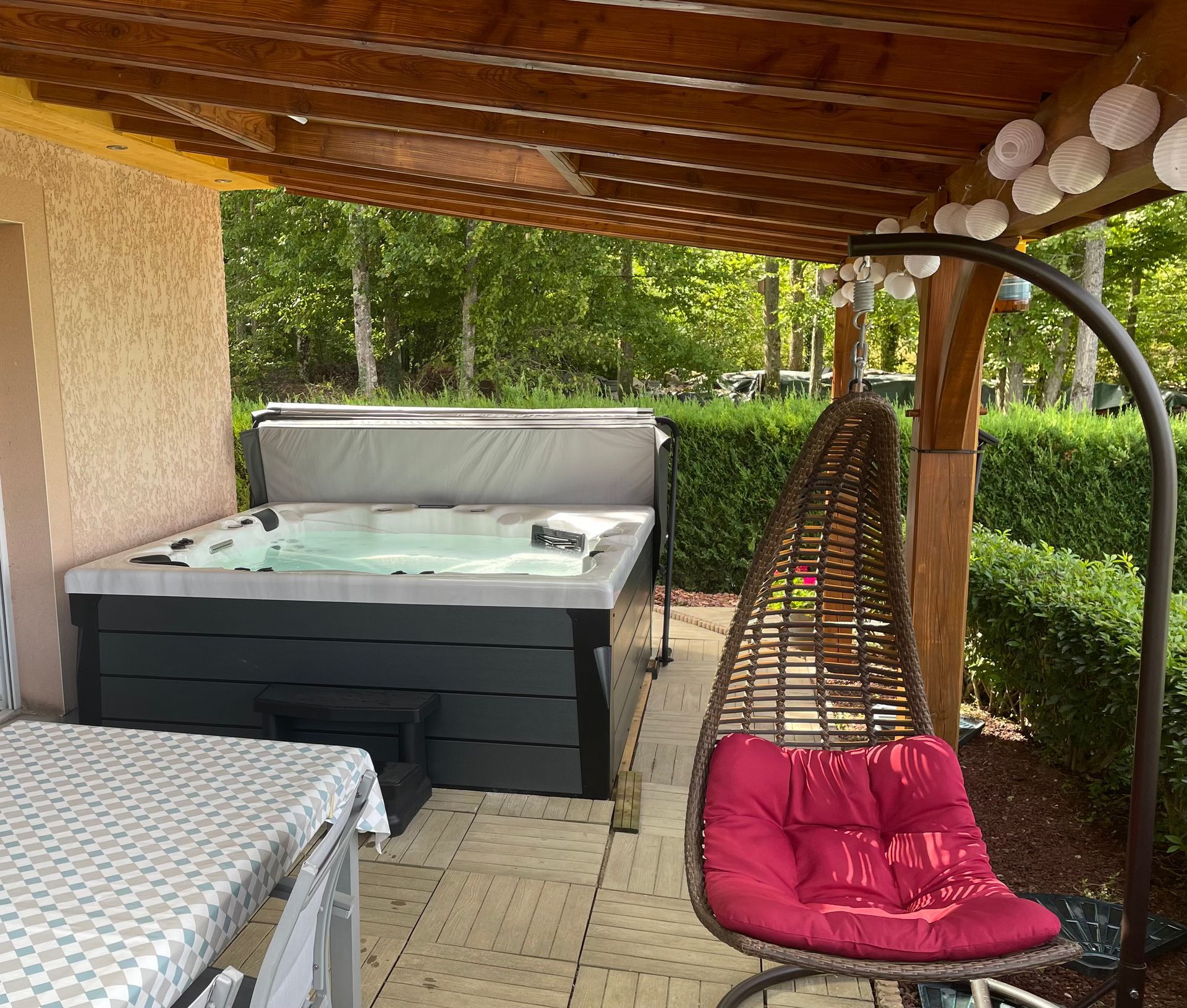 Un bain à remous est installé sous une pergola avec une chaise suspendue.