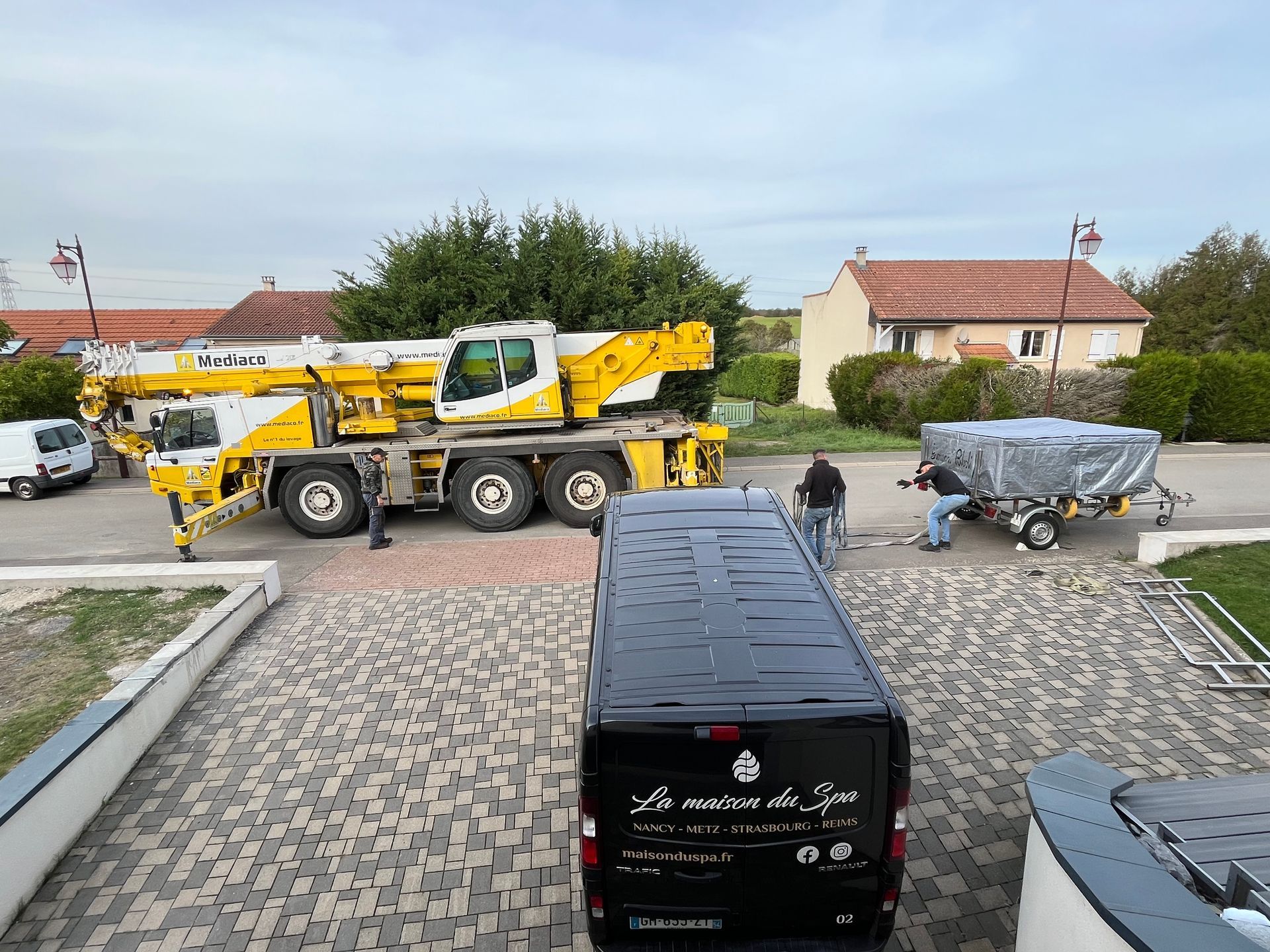 Une grande grue jaune est garée sur un parking à côté d'une camionnette noire.