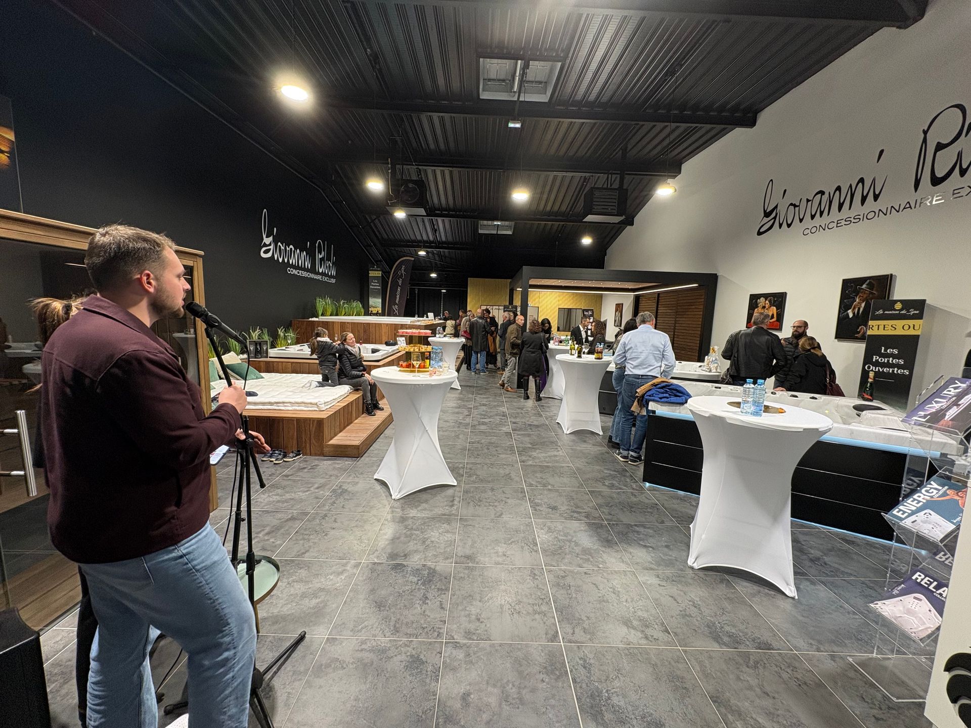 Un homme chantant avec un microphone lors d'un événement ; des gens assis à des tables de cocktails dans une salle.