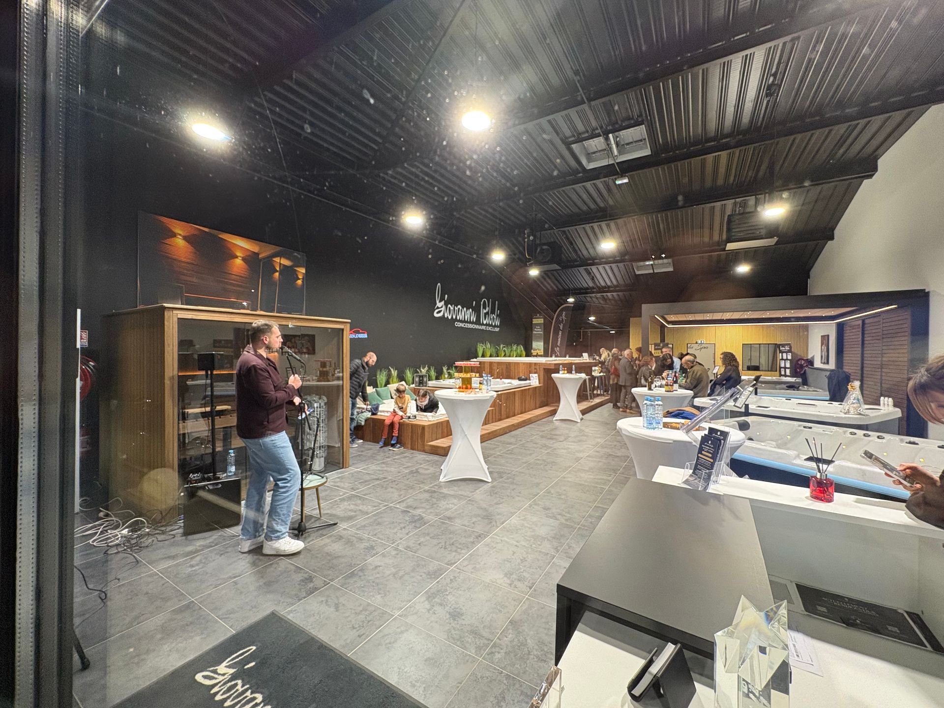 Intérieur d'un showroom moderne avec des personnes, des tables et des présentoirs de produits. Murs et éclairage sombres.