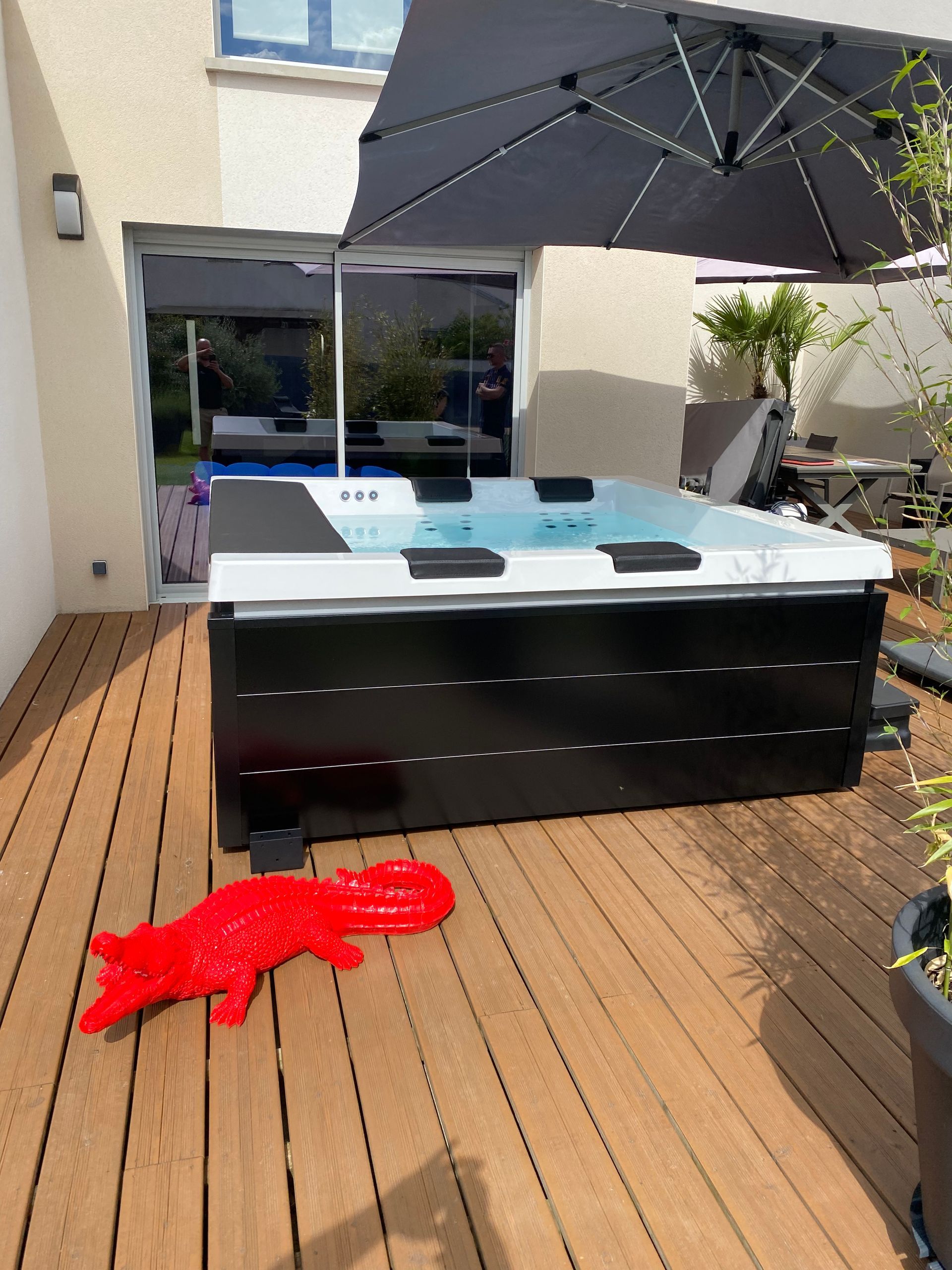Un jacuzzi noir et blanc est posé sur une terrasse en bois sous un parasol